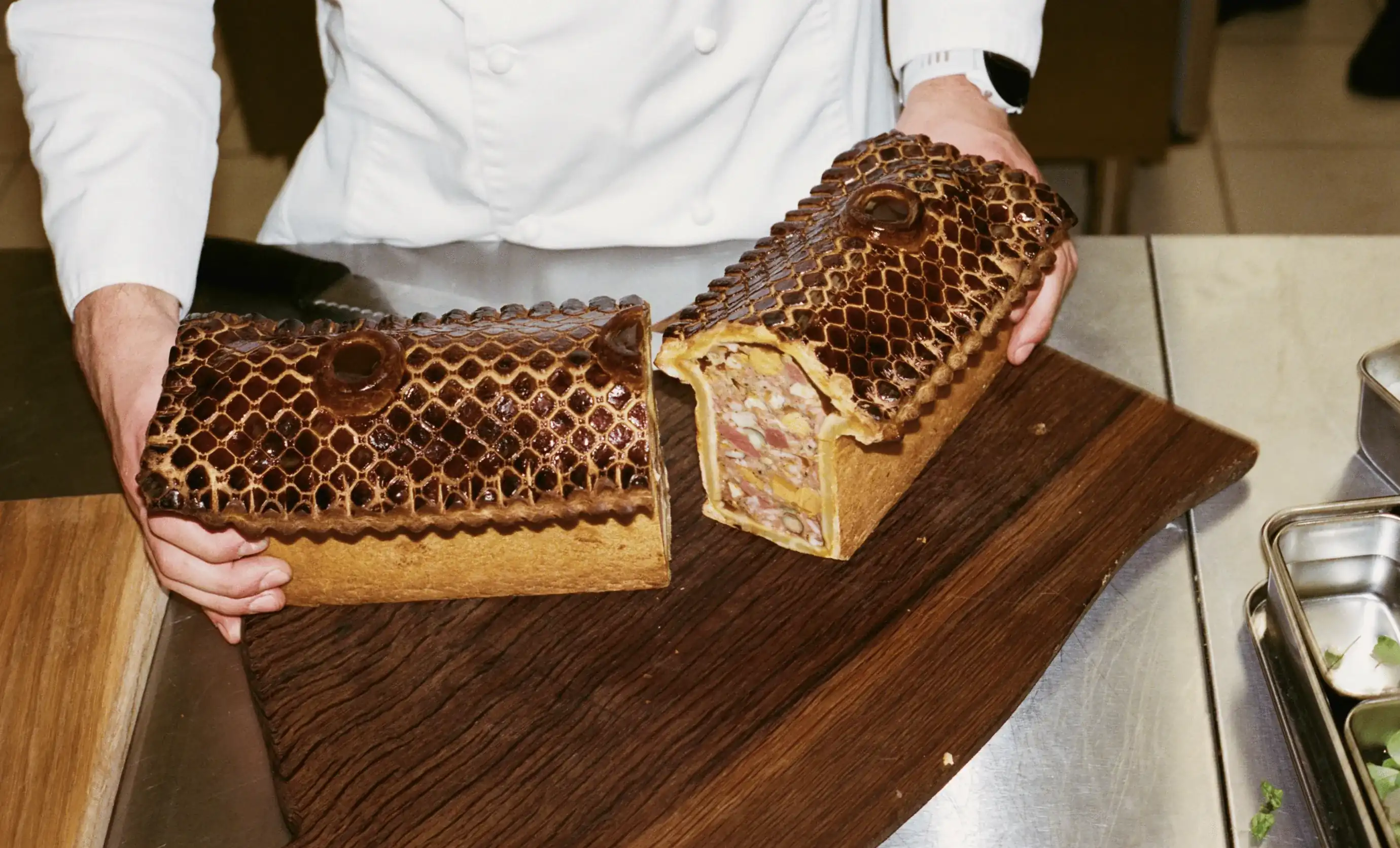 Chef segurando uma terrina de carne decorativa em forma de cabeça de réptil em uma tábua de madeira.