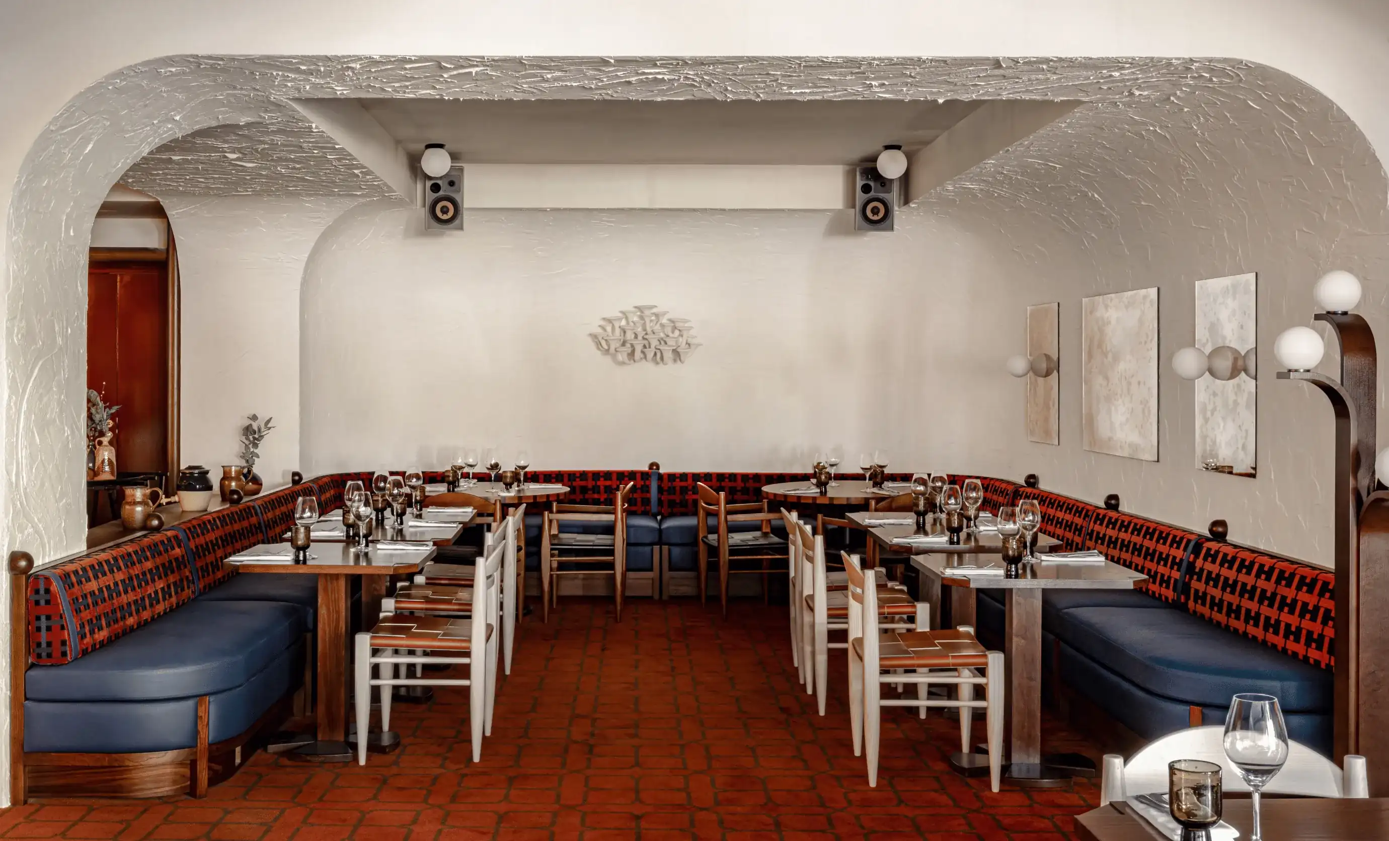 Interior aconchegante do restaurante com paredes brancas curvas, assentos para banquetes azuis e vermelhos e mesas arrumadas.