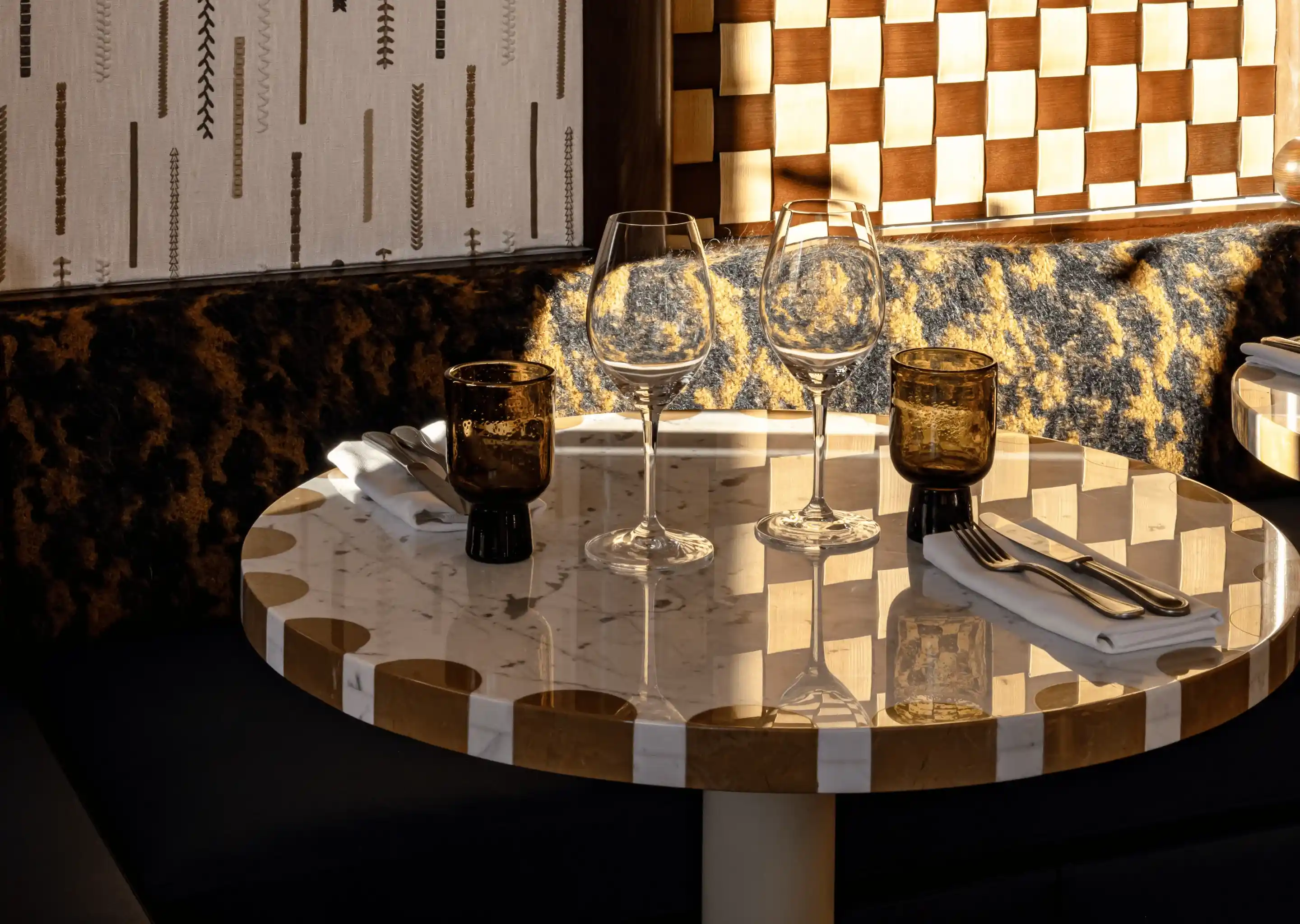Mesa redonda de mármore com duas taças de vinho vazias, duas taças de âmbar e talheres em guardanapos.