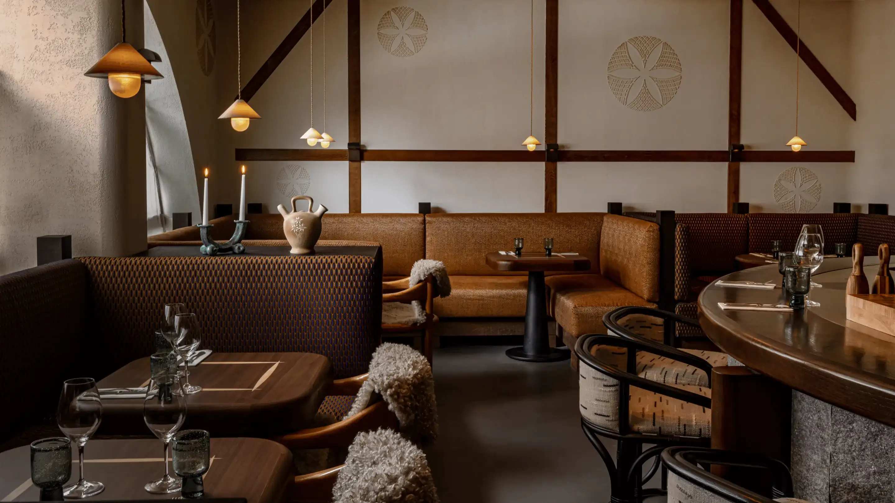 Interior aconchegante de restaurante com mesas de madeira, bancos almofadados e luminárias suspensas.
