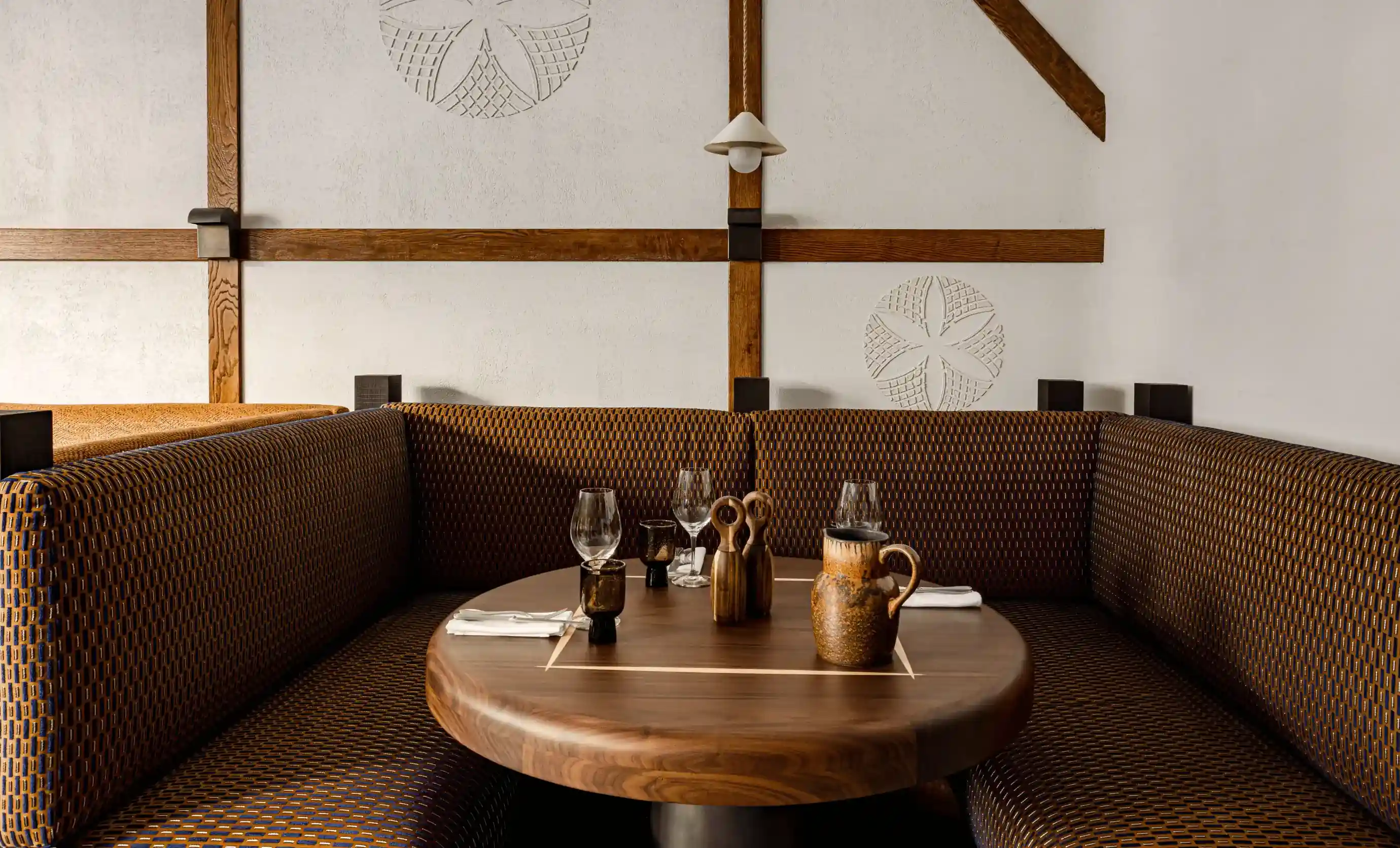 Mesa de madeira aconchegante com copos, jarros e utensílios em uma cabine de canto com estofamento estampado.