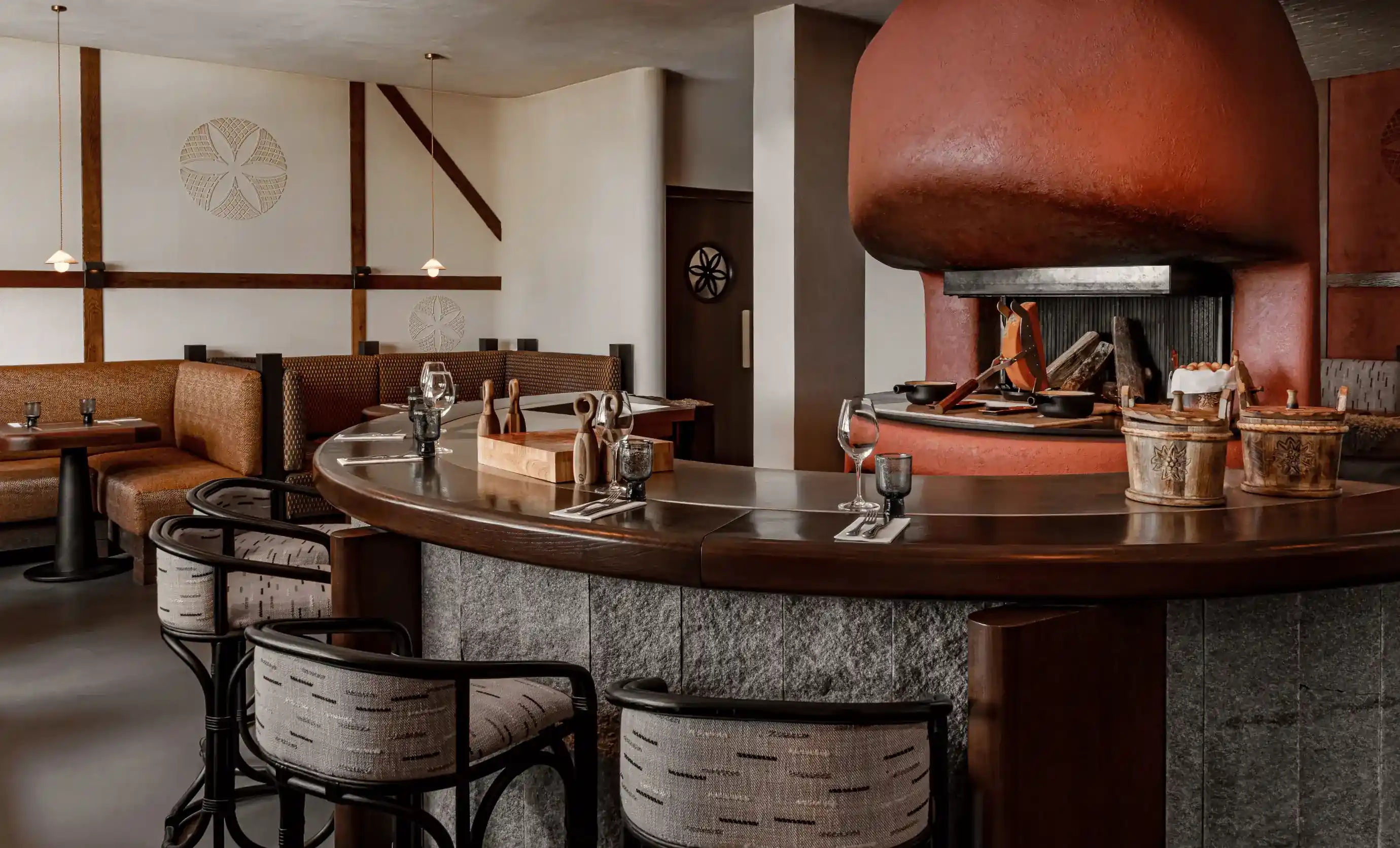 Bar curvo com copos e decoração de madeira ao redor de uma grande lareira avermelhada em uma aconchegante sala de restaurante.