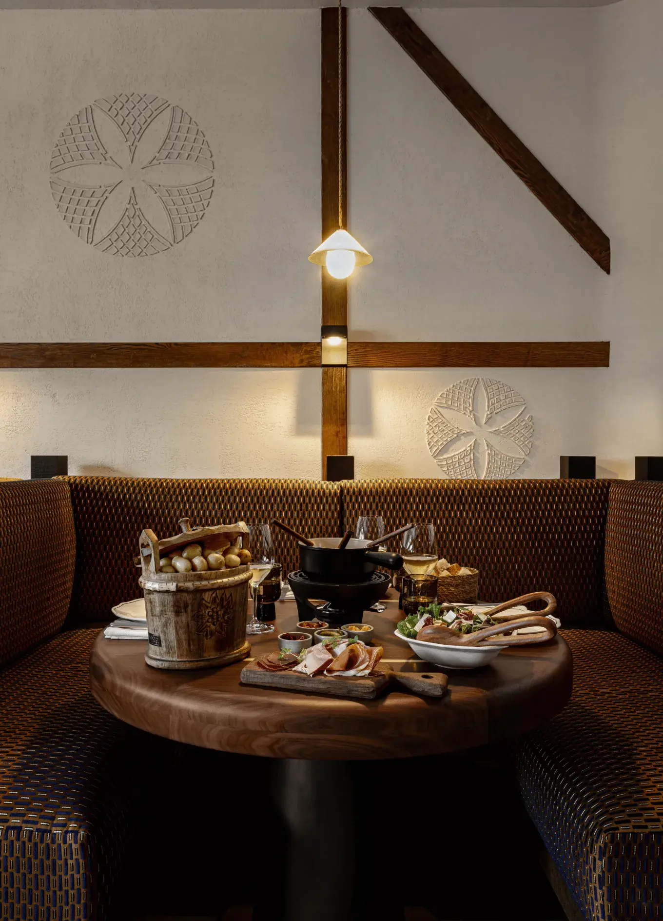 Restaurante aconchegante com bancos estampados, mesa de madeira com fondue, salada e taças de vinho.