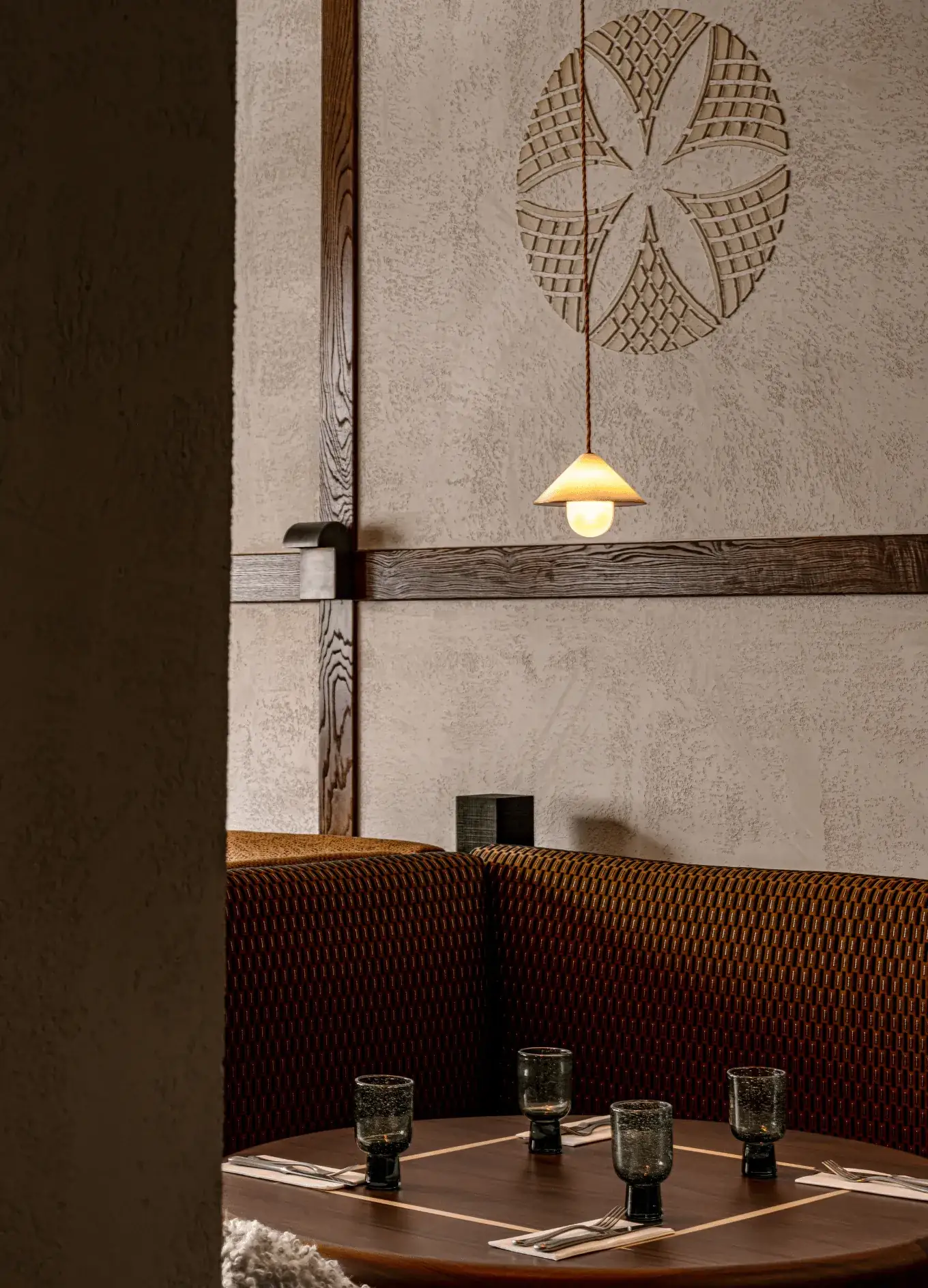 Cozy restaurant booth with patterned seats, wooden table set with glasses and napkins, and warm pendant light.