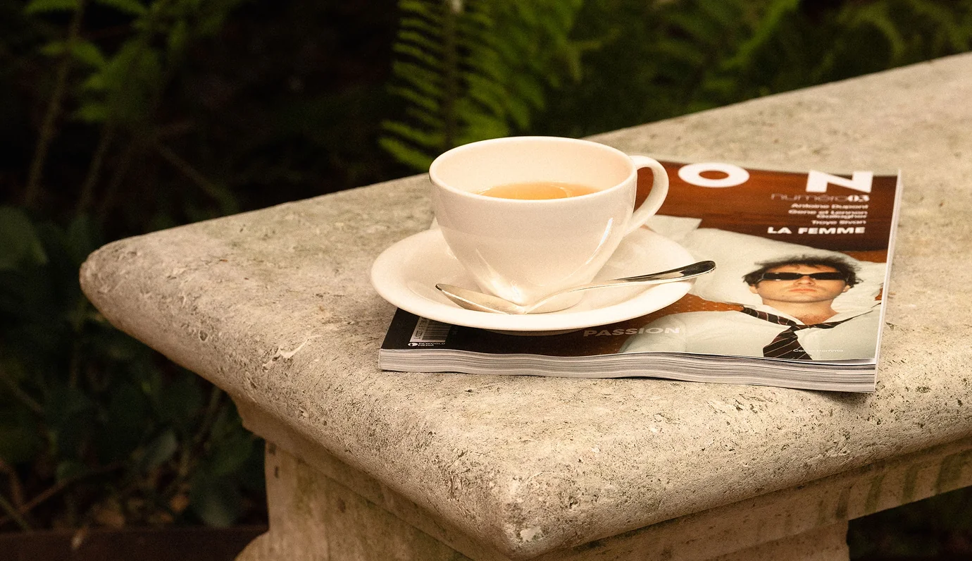 Tazza da tè bianca con piattino e cucchiaio su una rivista in cima a un tavolo di pietra all'aperto.