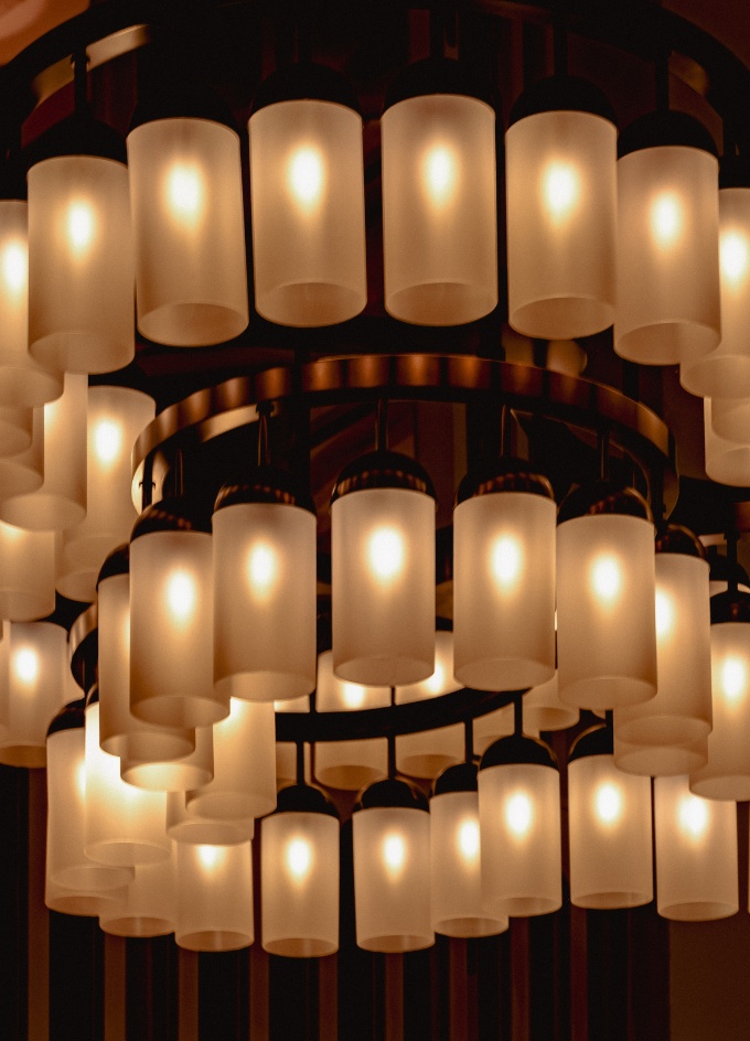 Lampadario moderno circolare con più paralumi cilindrici in vetro satinato a luce calda.