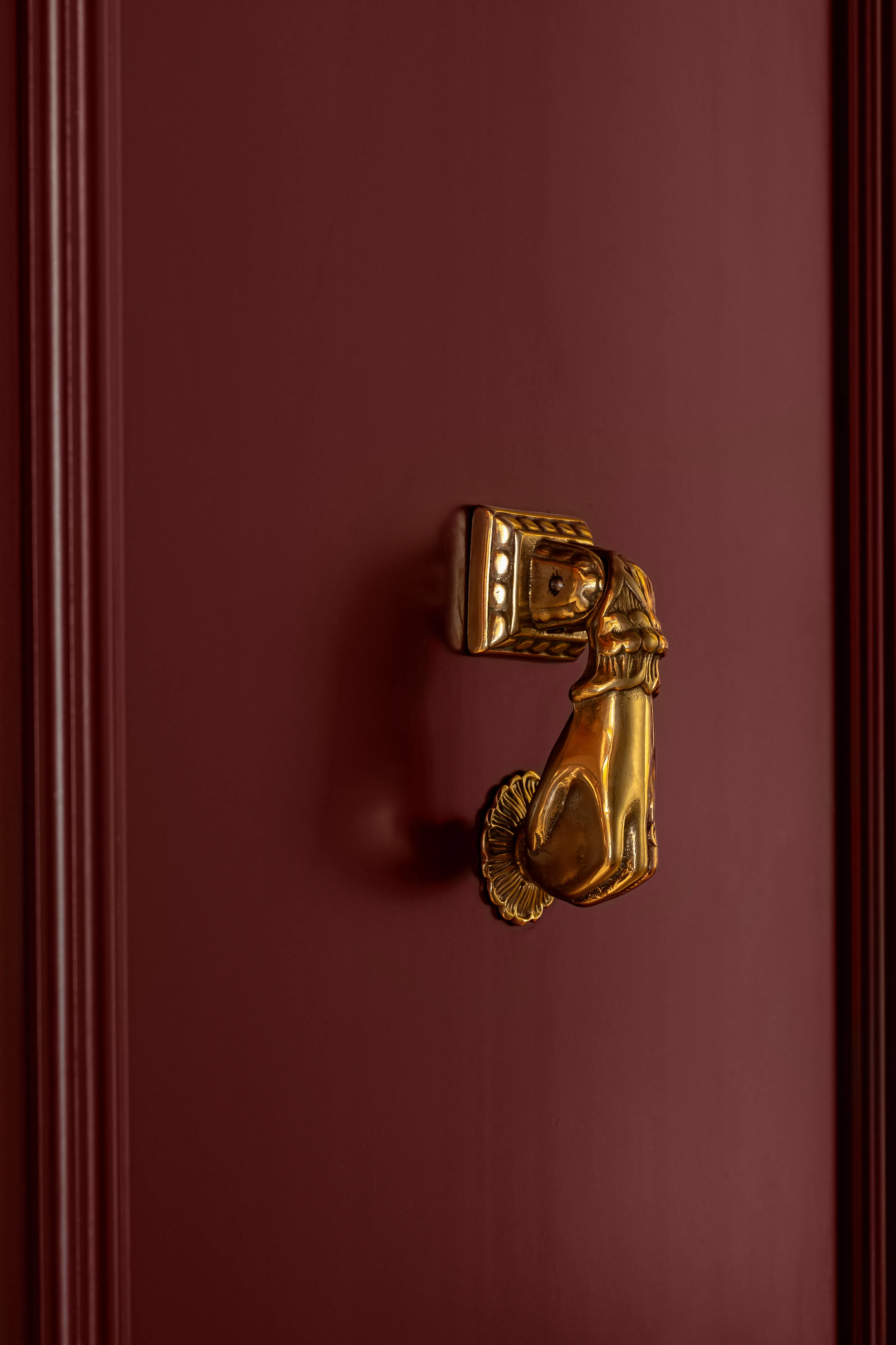 Battente a forma di mano color oro montato su una porta in legno rosso scuro.