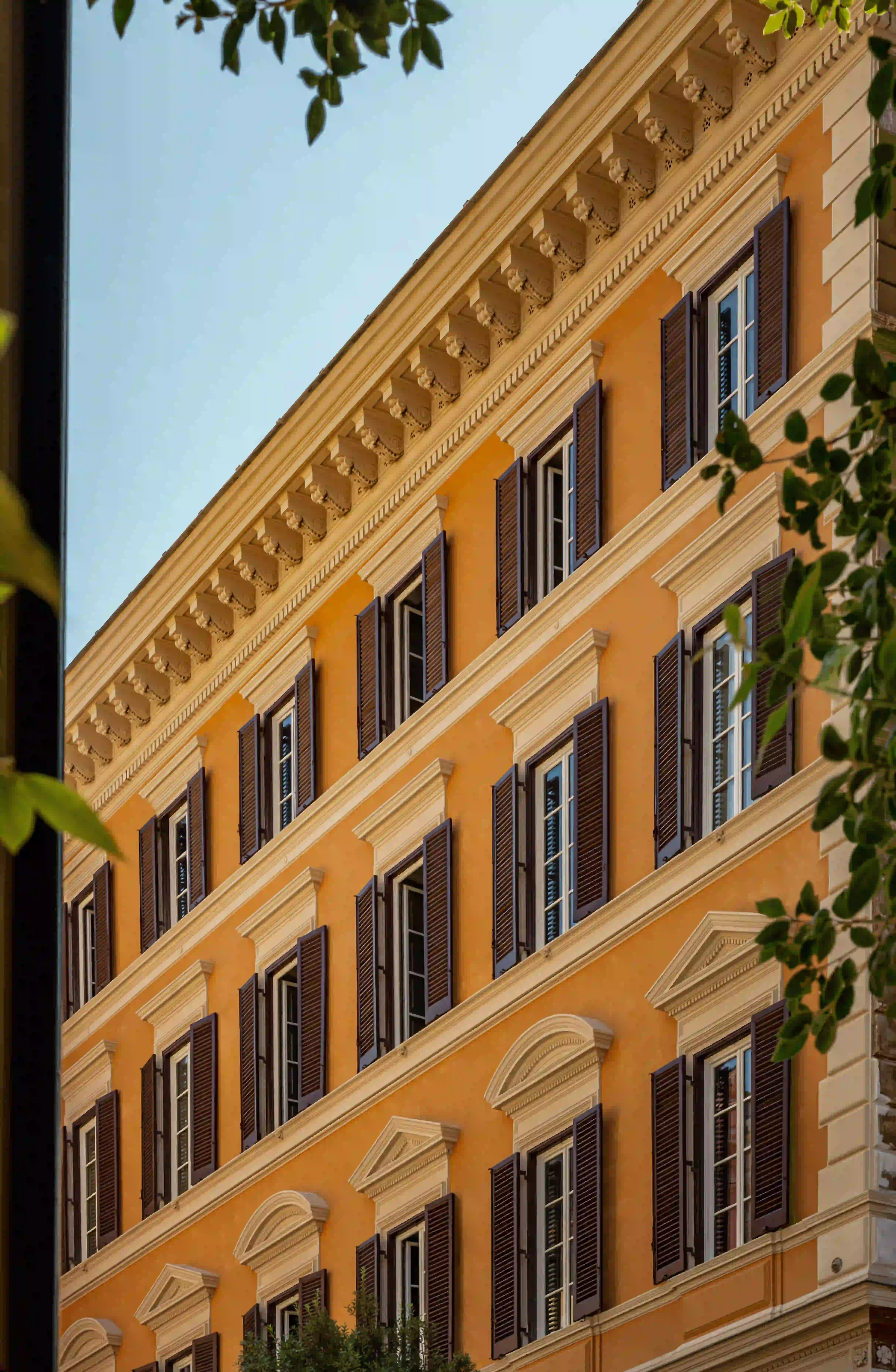 Facciata arancione di un edificio italiano con finestre simmetriche, persiane scure e dettagli architettonici decorati.