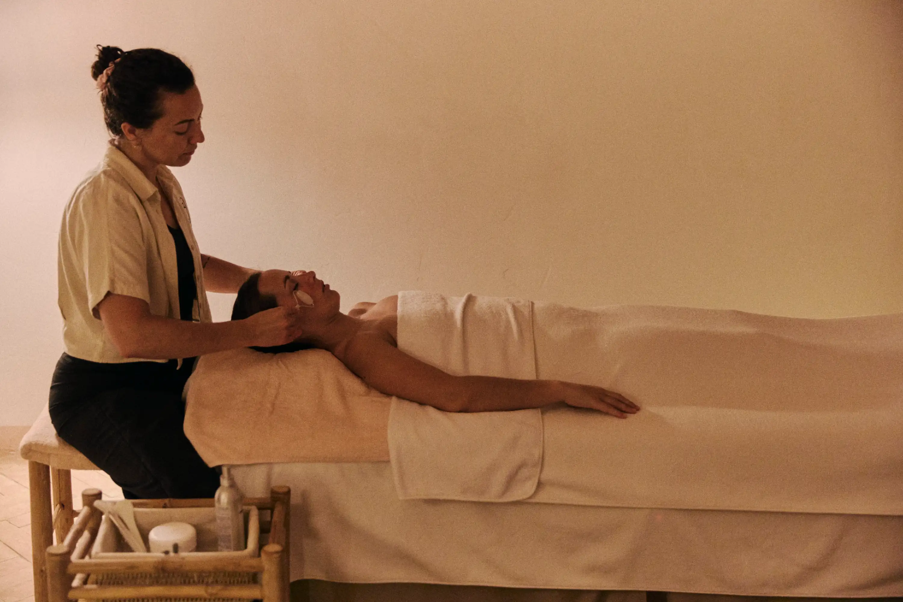 Mulher recebendo uma massagem facial do terapeuta em uma sala de spa calma e suavemente iluminada.