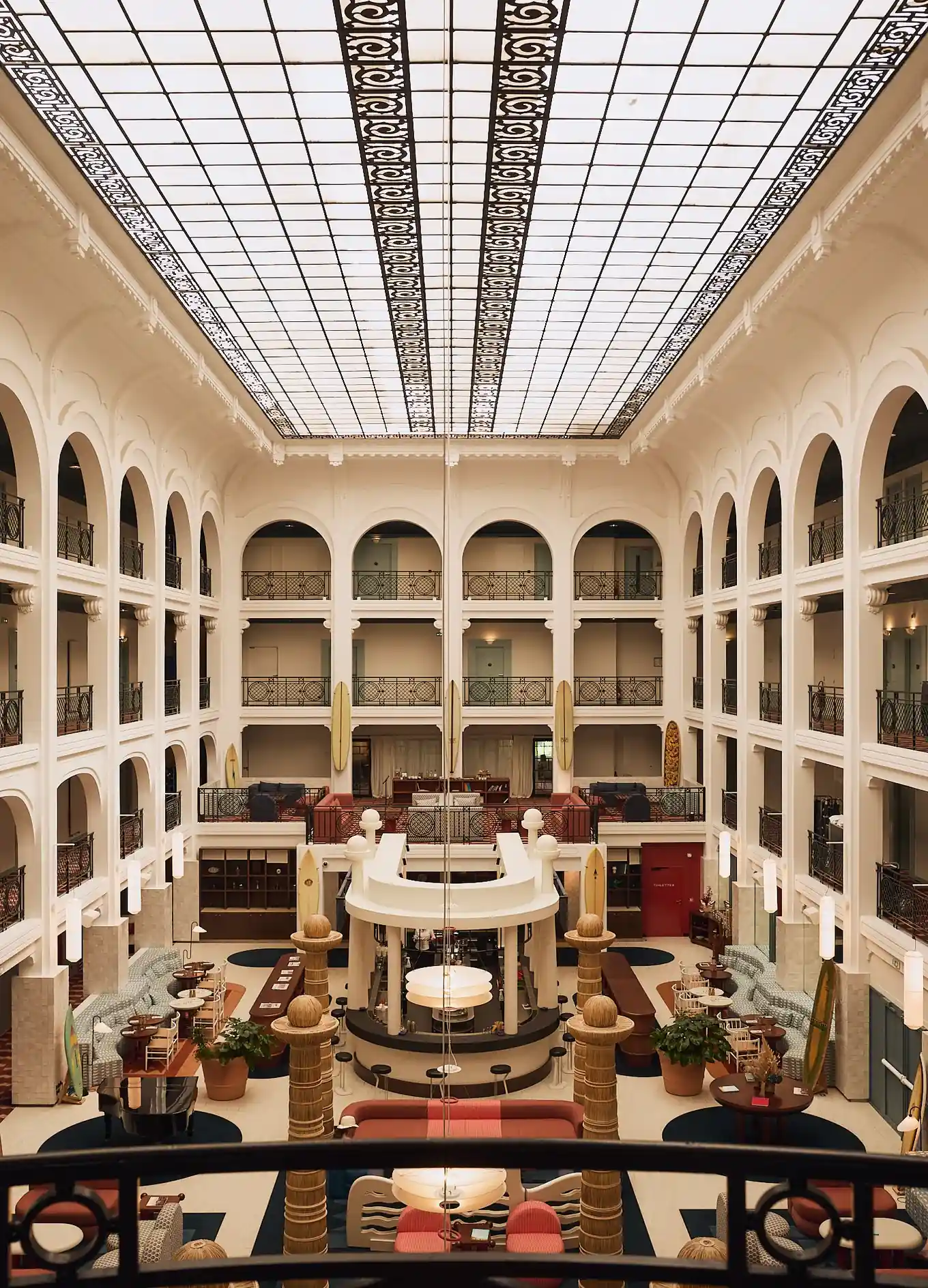 Spacious hotel lobby with high glass ceiling, arches, seating areas, and artistic columns.