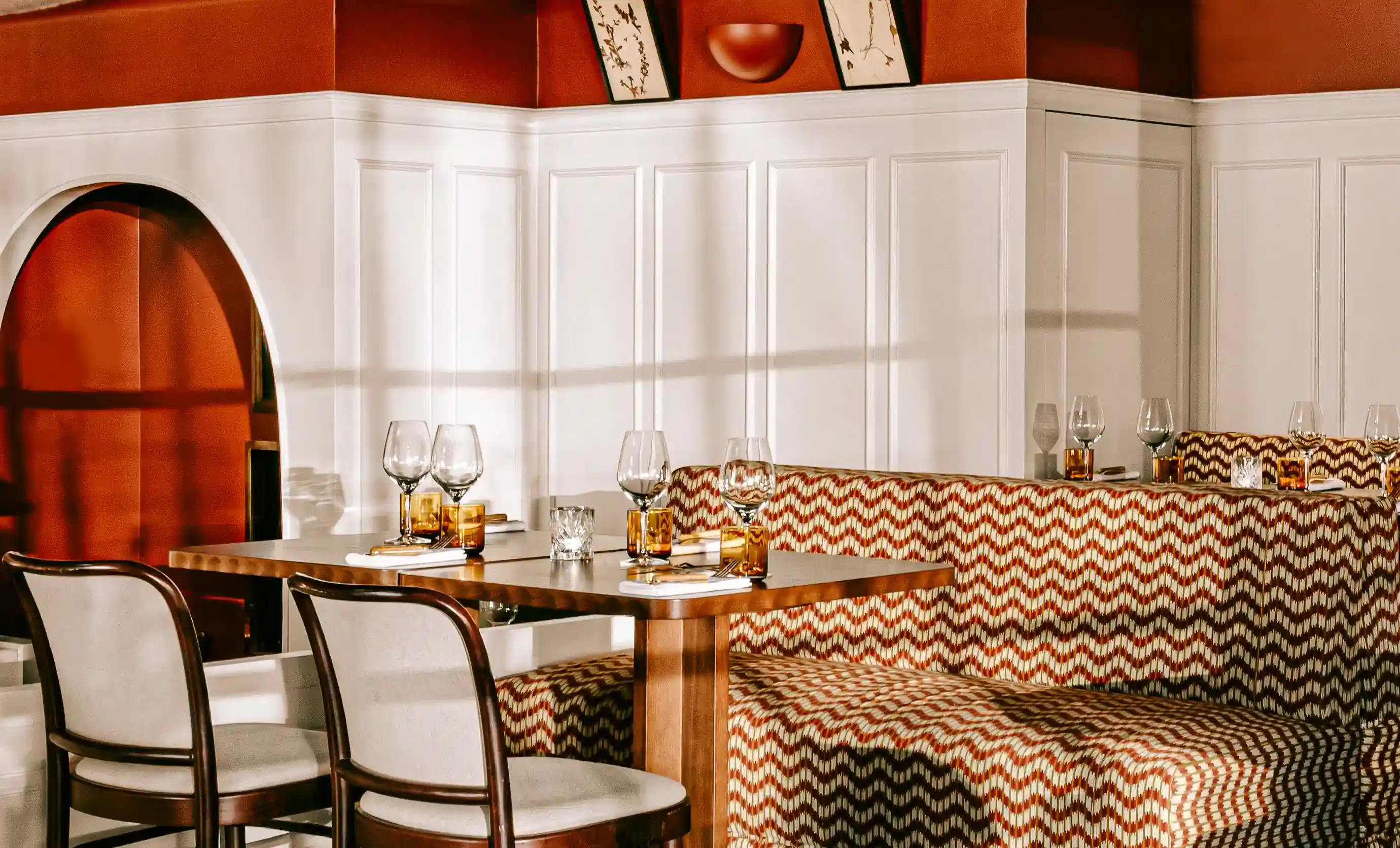 Dining area with wooden table, patterned cushioned bench, white chairs, and set glassware.