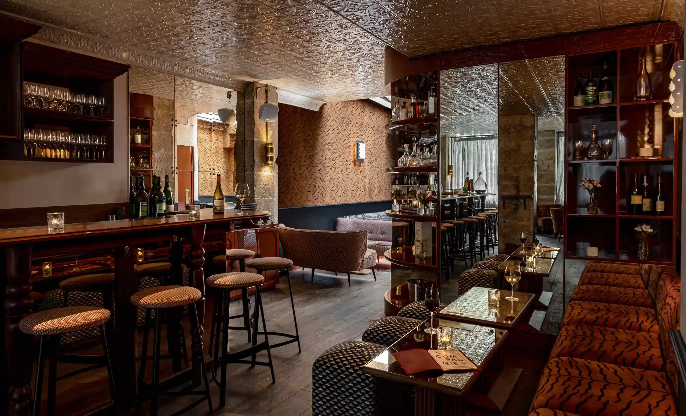 Accogliente bar e lounge con sgabelli a motivi geometrici, pareti a specchio, panche imbottite e bottiglie sugli scaffali.