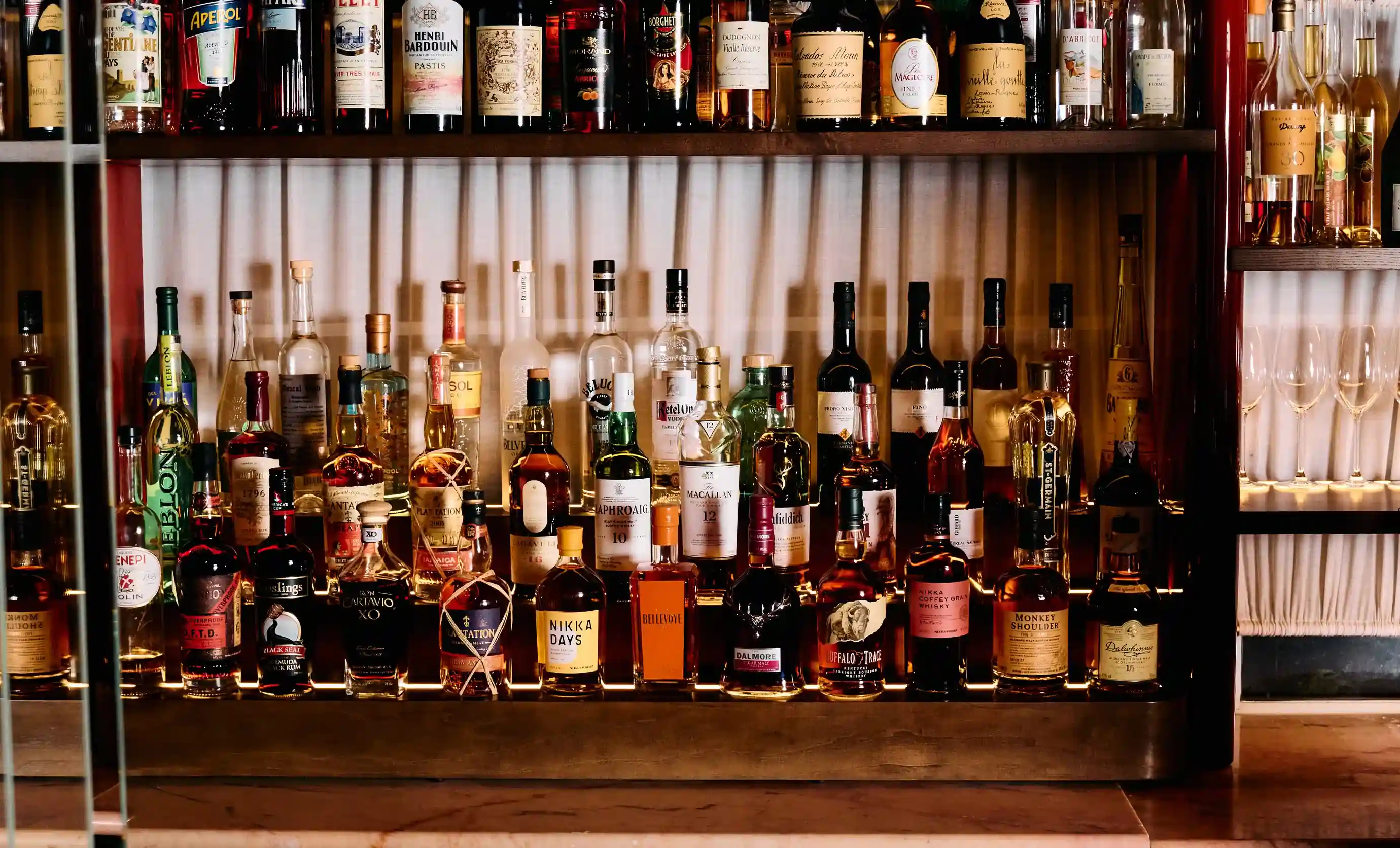 A well-stocked bar shelf displaying various liquor bottles and glassware with warm lighting.