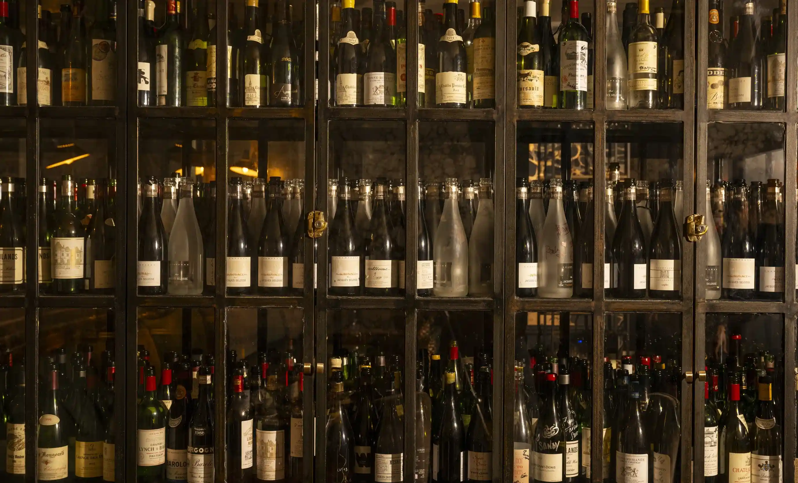 Mobile con facciata in vetro pieno di molte bottiglie di vino sugli scaffali all'interno di una stanza poco illuminata.