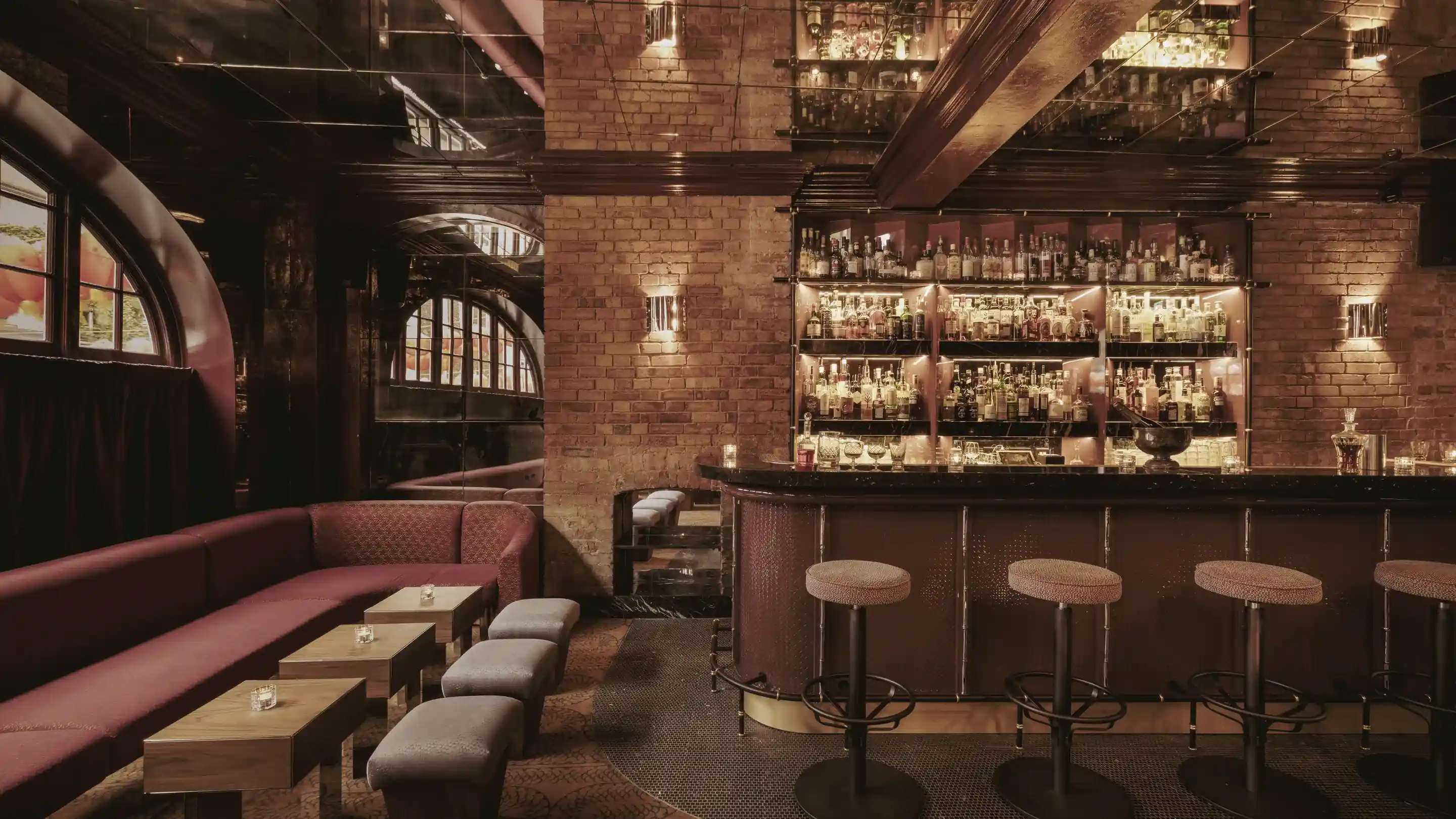 Cozy bar interior with brick walls, bar stools, wooden tables, and a long upholstered bench.