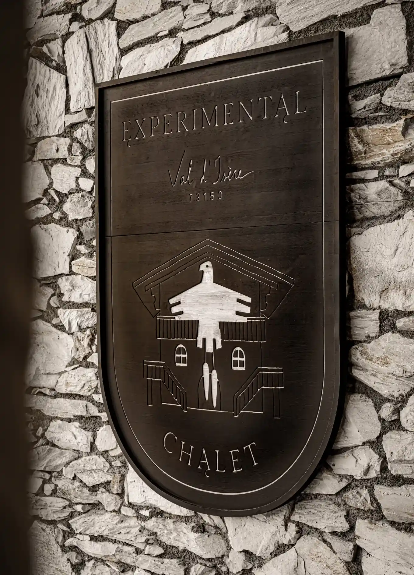 Cartel de madera que dice Experimental Chalet Val d'Isere 73150 montado en una pared de piedra.