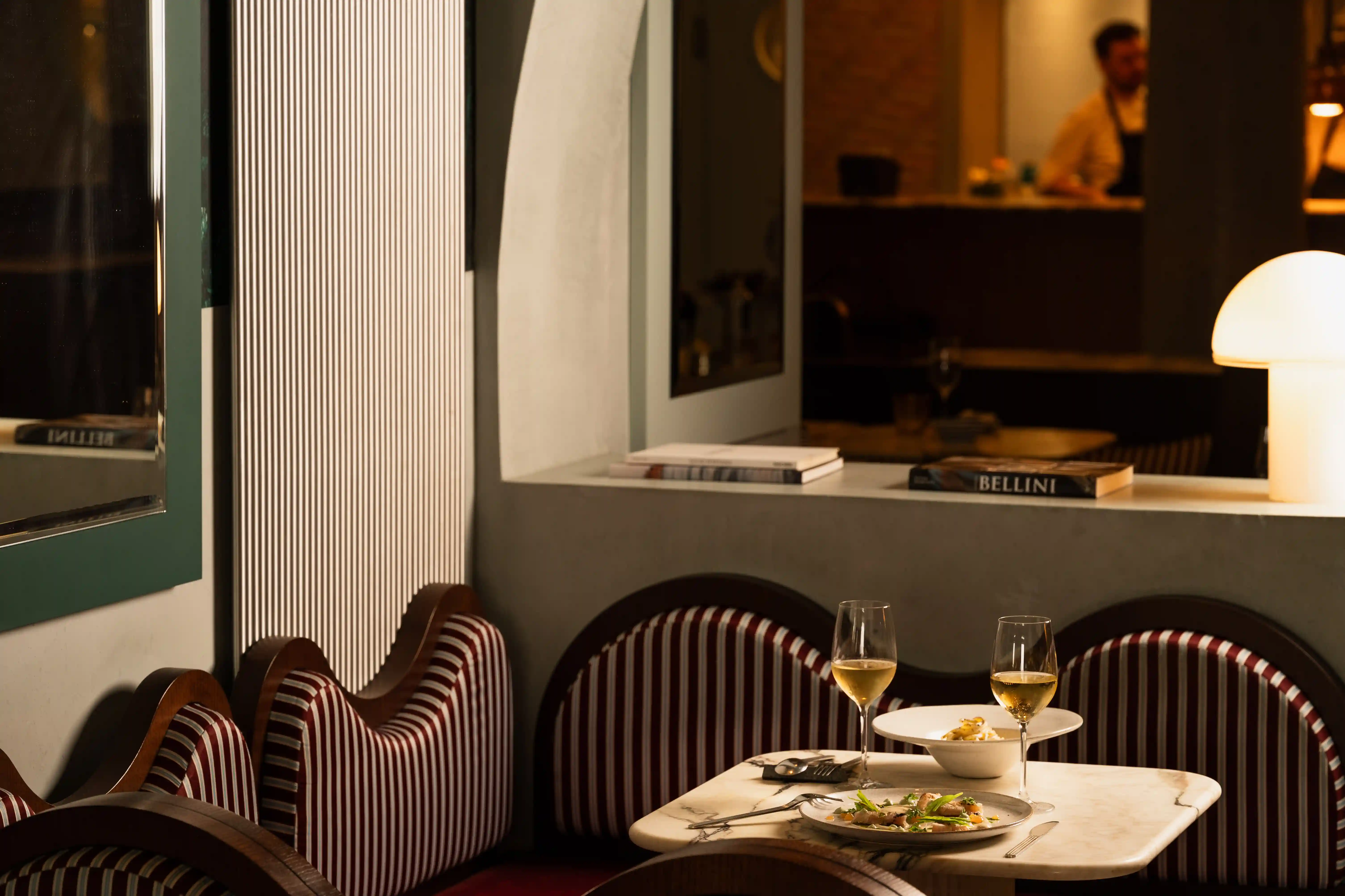Cozy restaurant table with two wine glasses, food plates, striped cushioned chairs, and warm lighting.