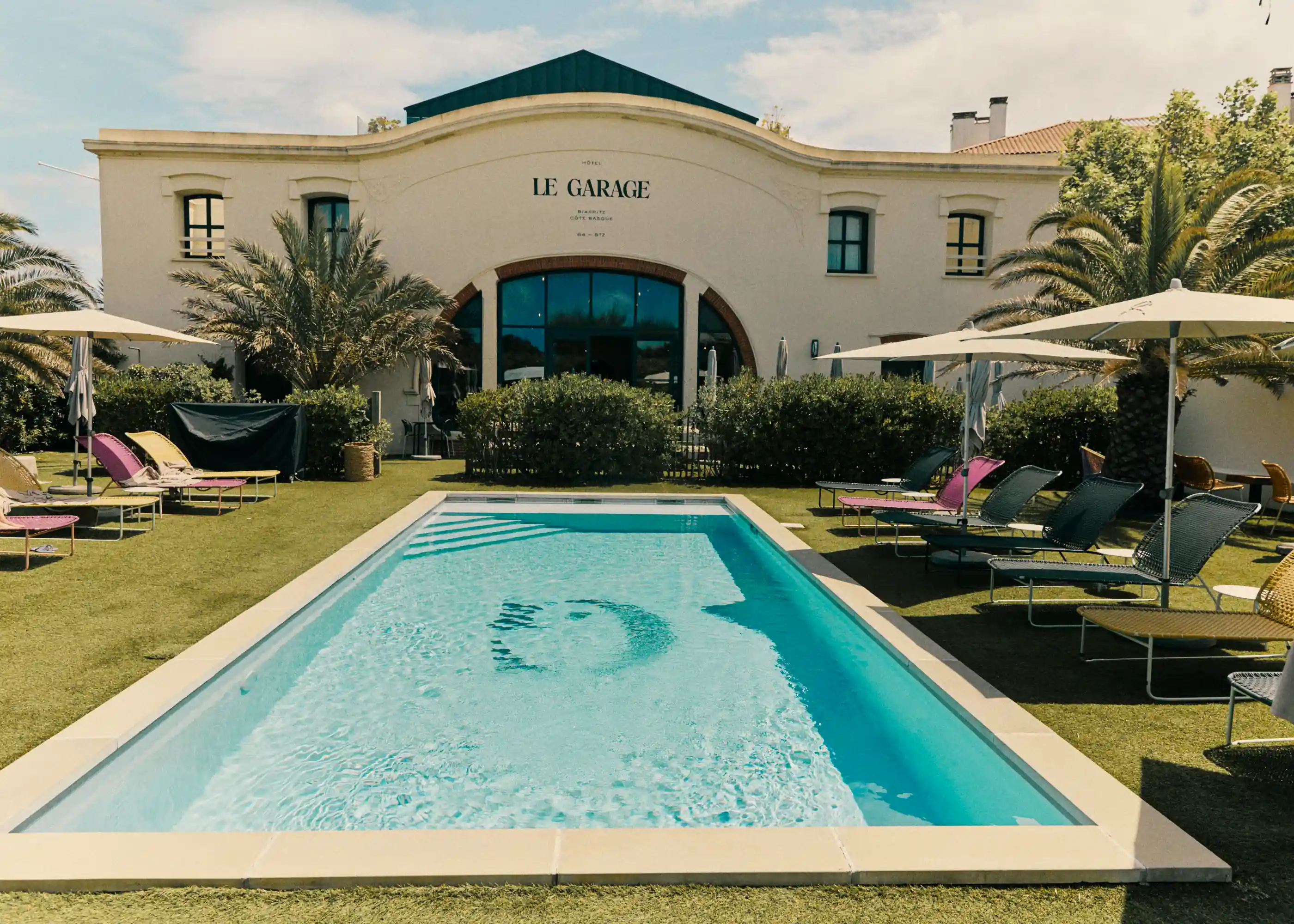 Outdoor swimming pool with lounge chairs and umbrellas in front of a building named Le Garage.