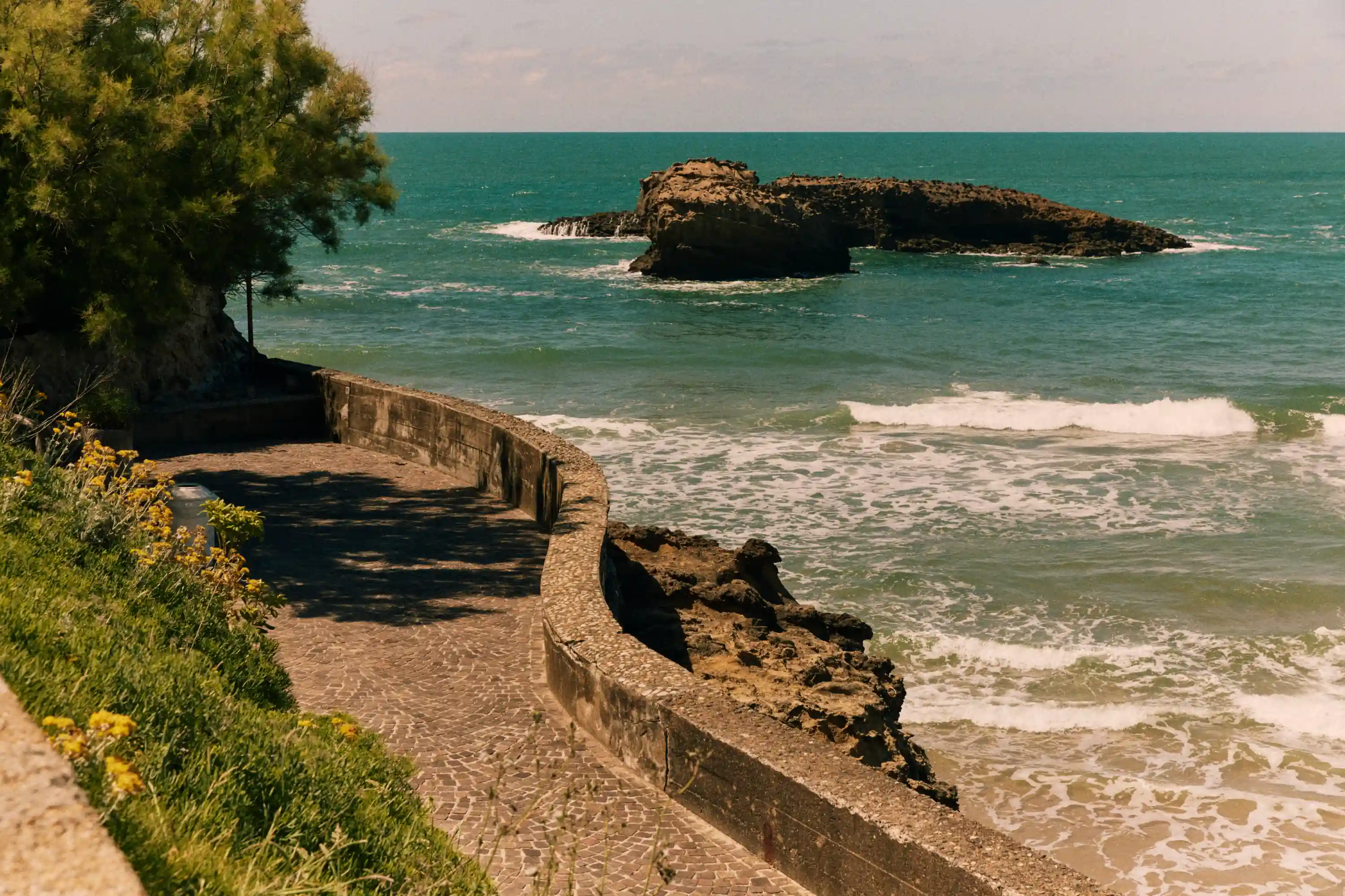 Coastal pathway with stone walls beside the ocean and rocky islets in the water.
