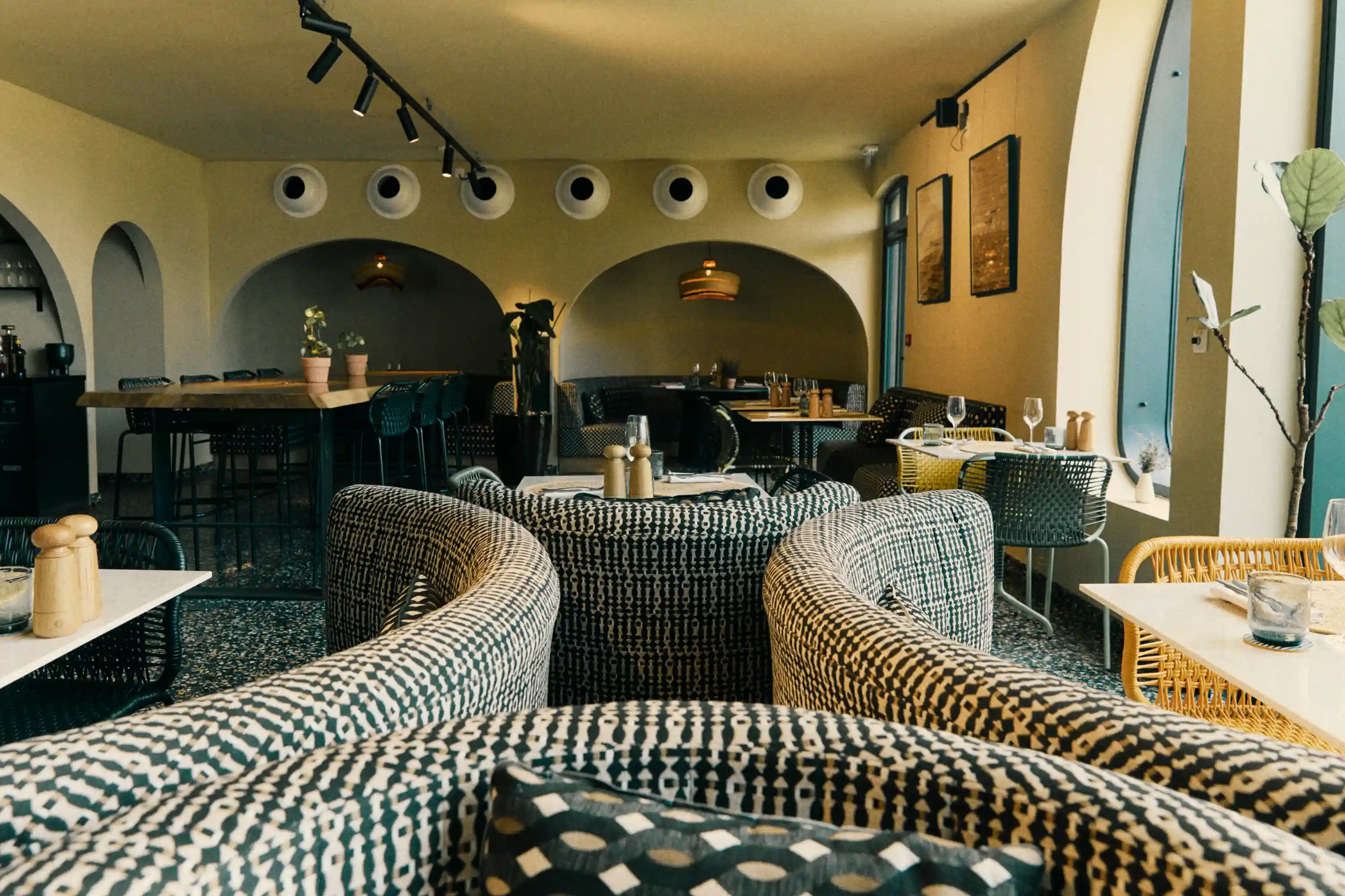 Cozy restaurant interior with patterned curved booths, tables, chairs, and warm ambient lighting.