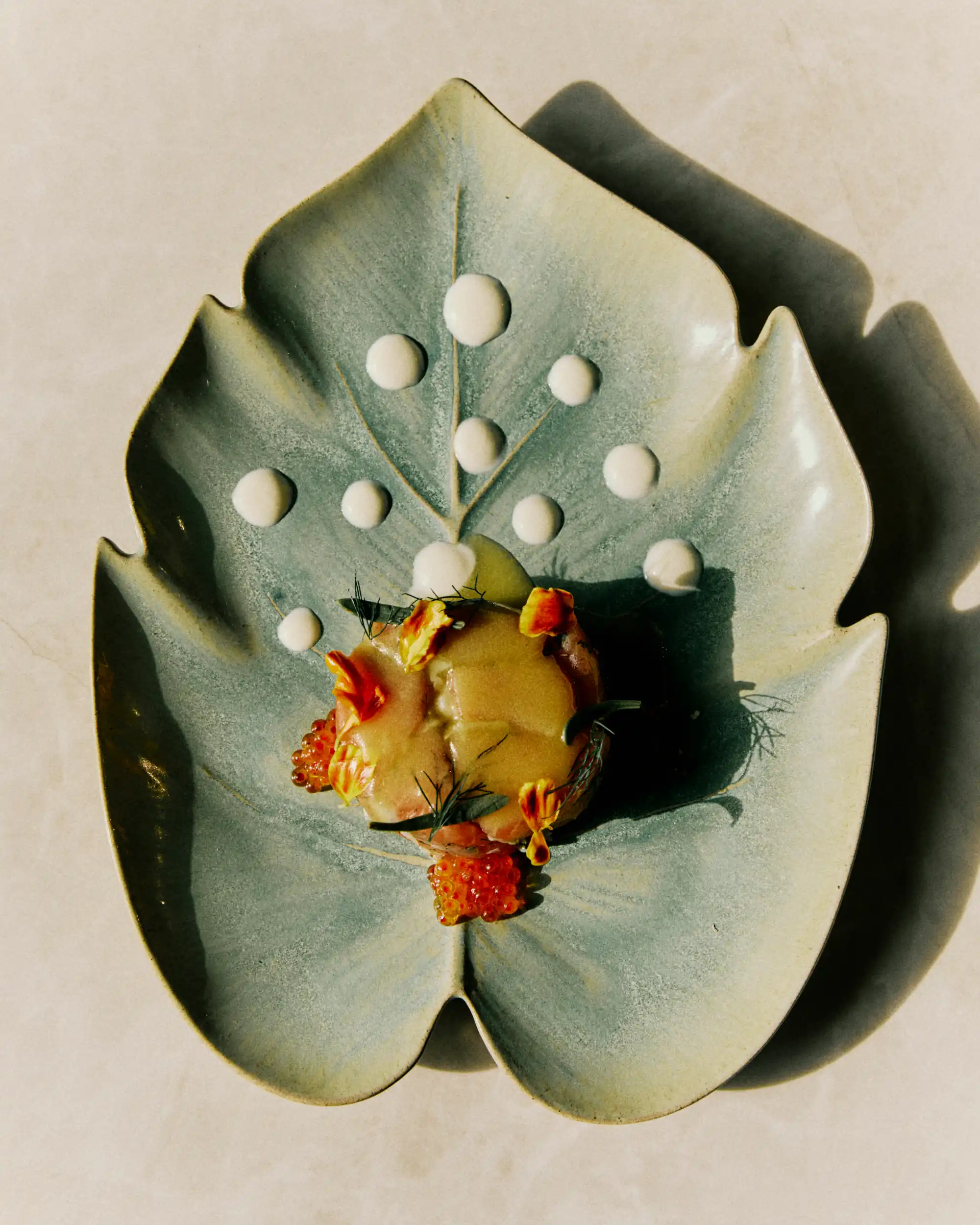 Leaf-shaped ceramic plate with a gourmet dish garnished with sauce drops and edible flowers.