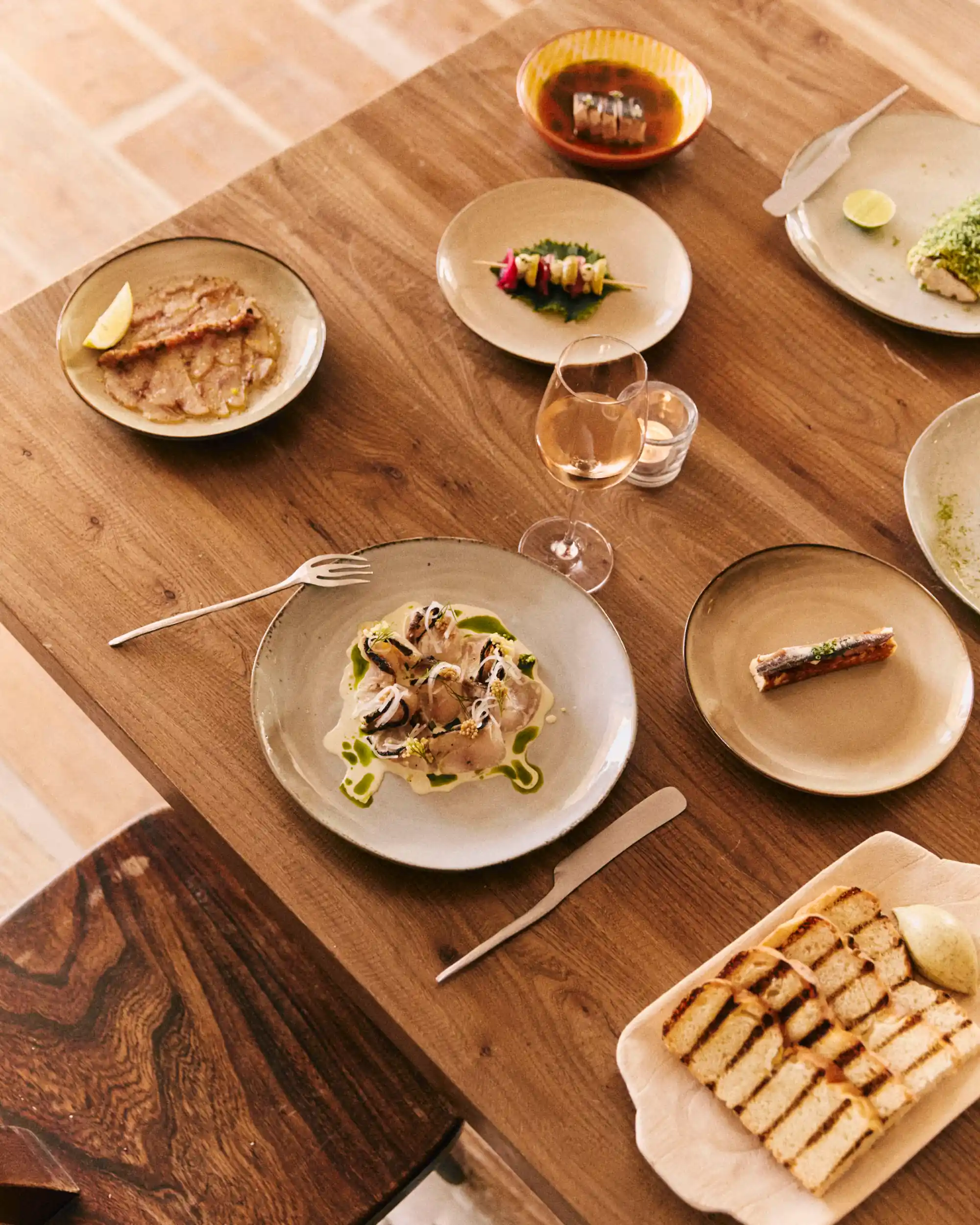 Wooden table with plates of gourmet dishes, a glass of rosé wine, and grilled bread with spread.