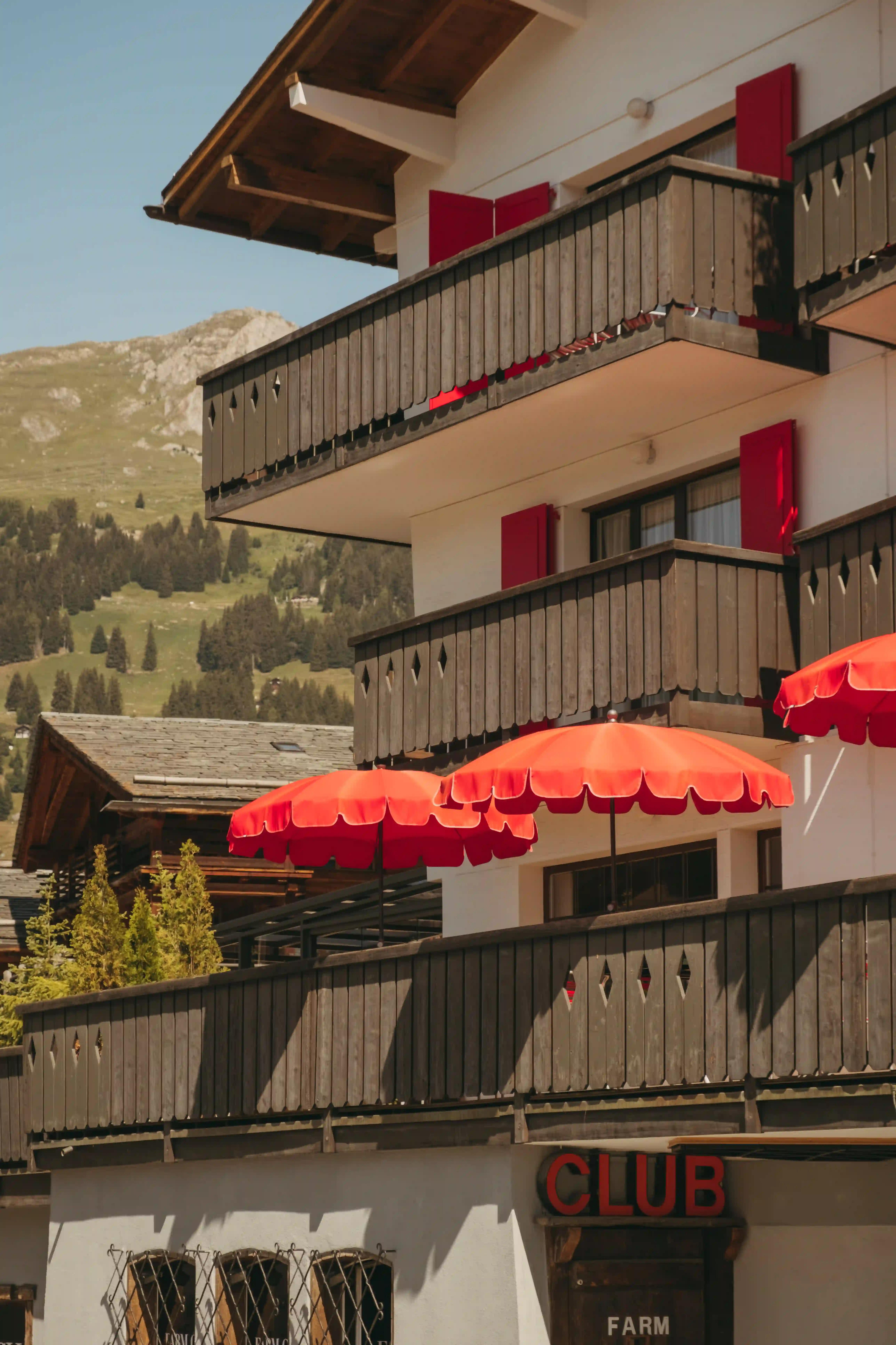 Balconies with red shutters and umbrellas on a mountain-side building under clear sky.