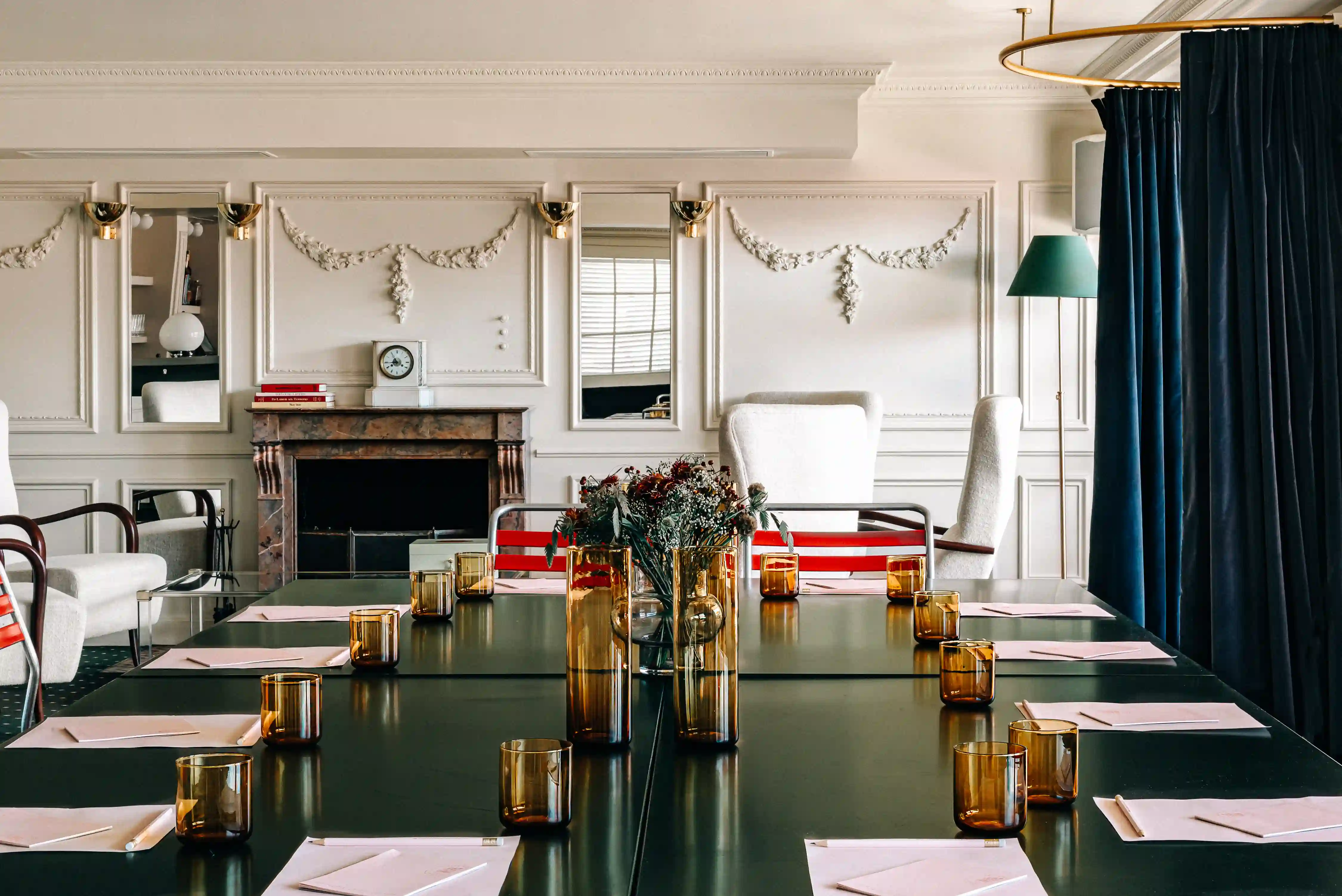 Elegant meeting room with green table, amber glasses, notepads, white chairs, and decorative wall moldings.