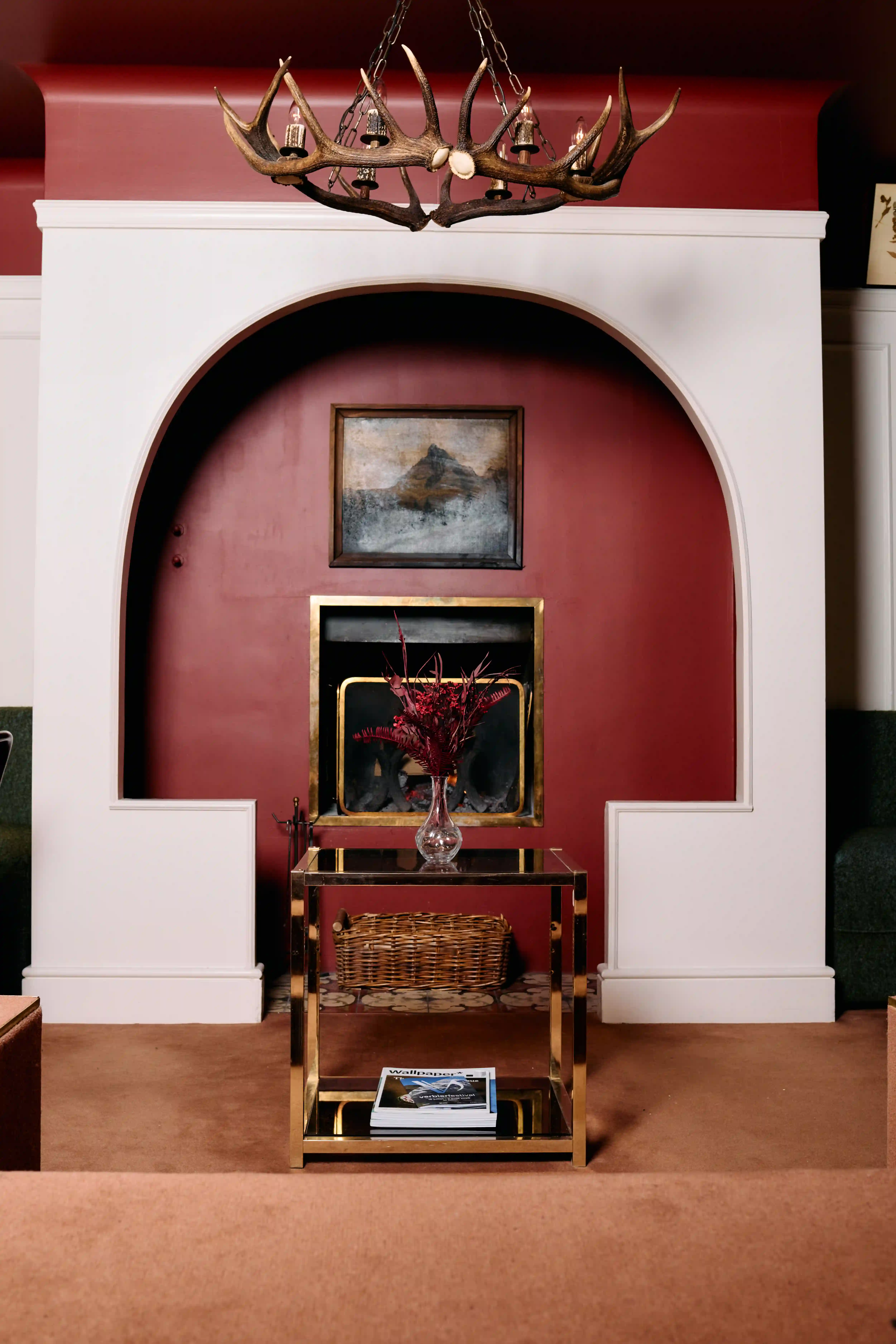 Cozy living room with red arched fireplace, antler chandelier, glass table, and basket underneath.