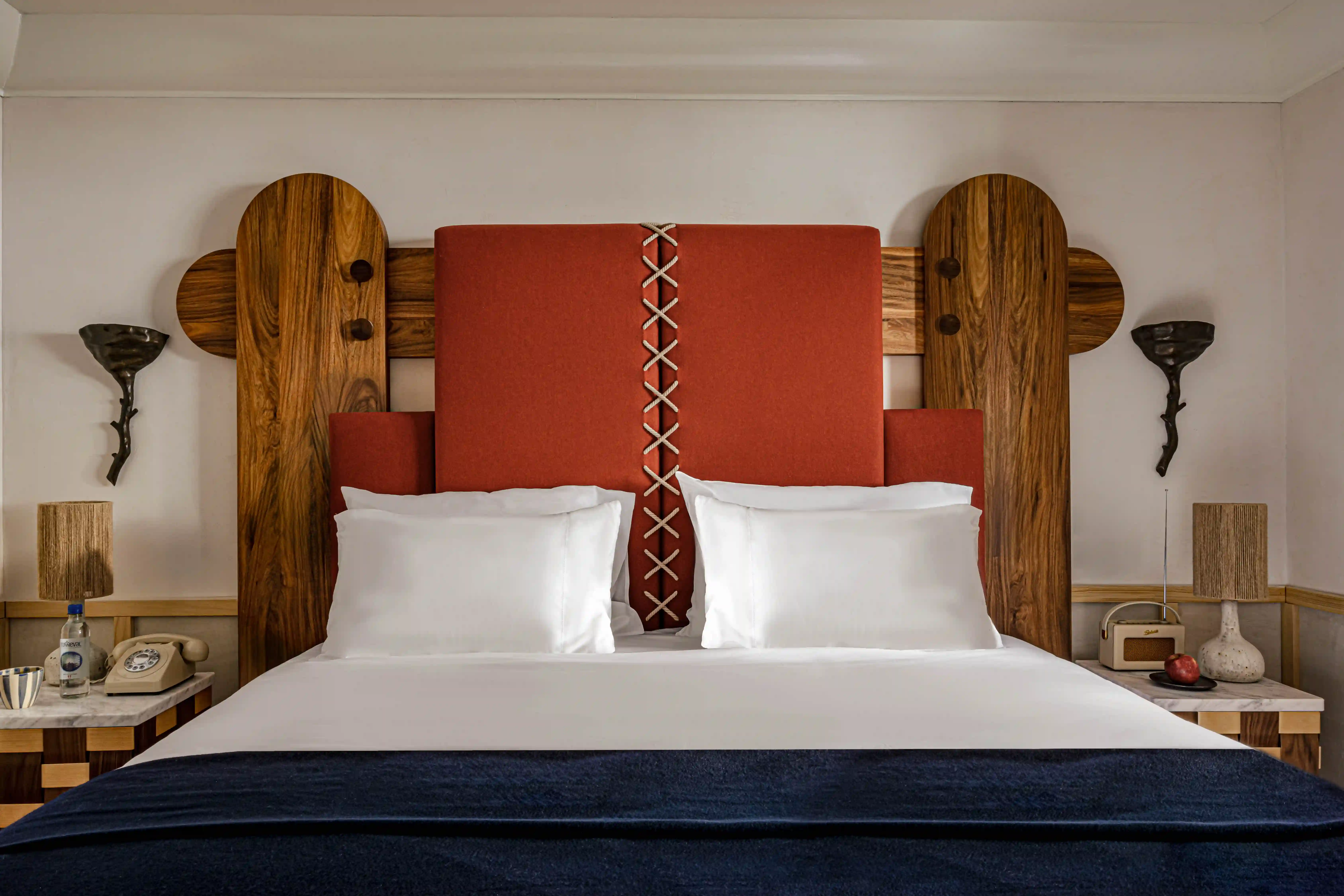 Stylish bed with large wooden headboard, orange cushioned center, white pillows, and navy blanket.