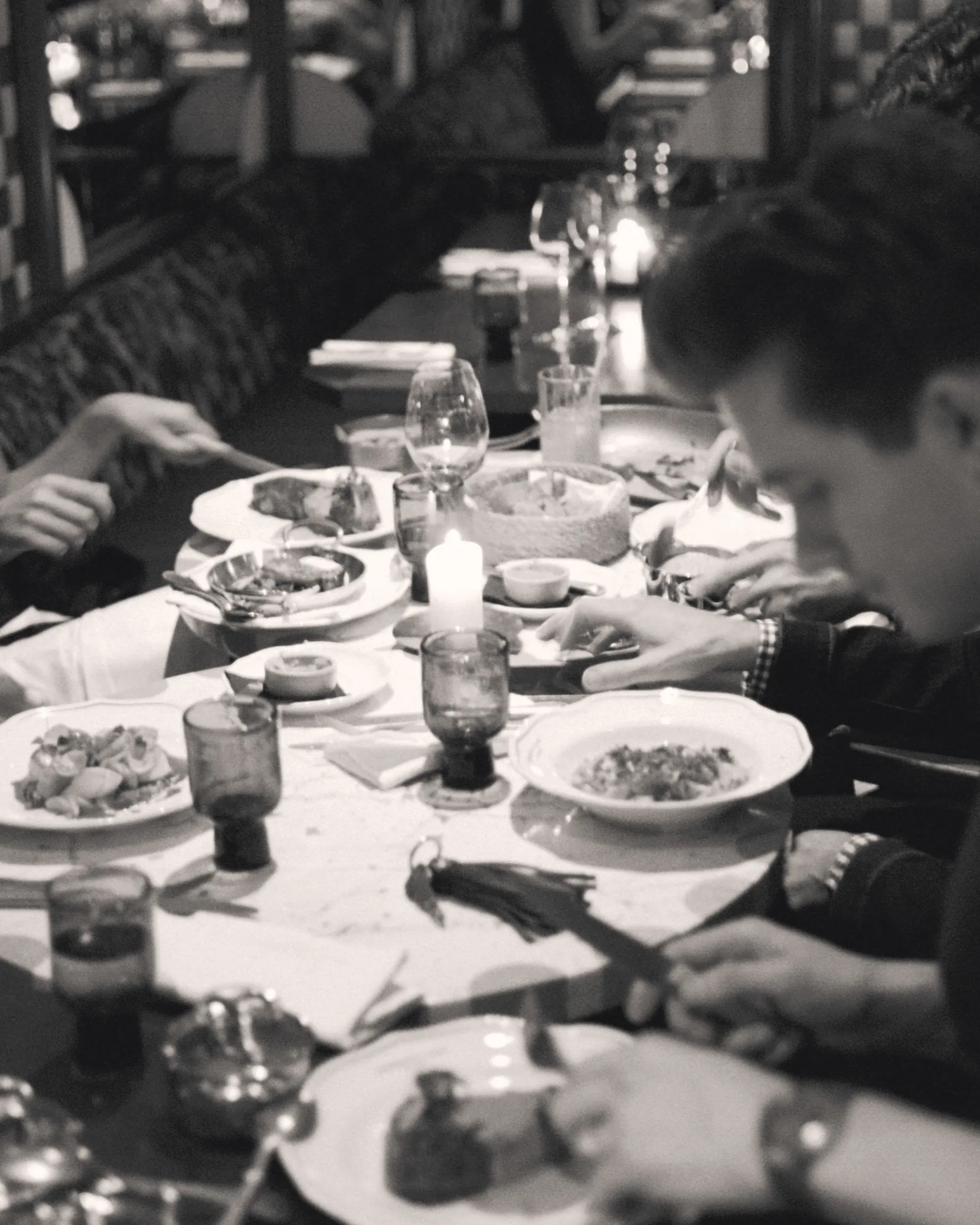 People dining at a restaurant table with plates, glasses, and a lit candle in black and white.