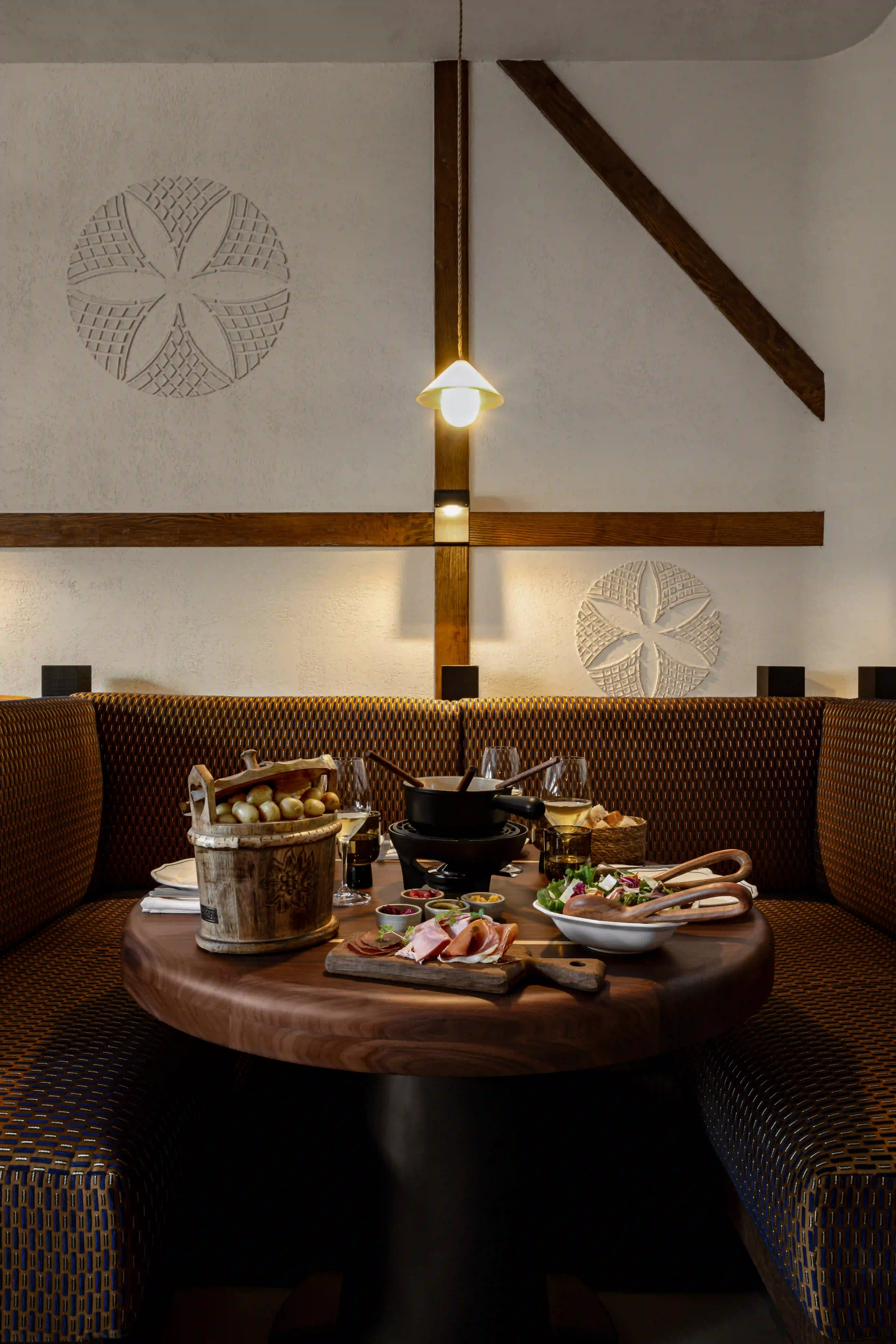 Cozy restaurant booth with rustic wood table set with fondue pot, meats, salad, and wine glasses.