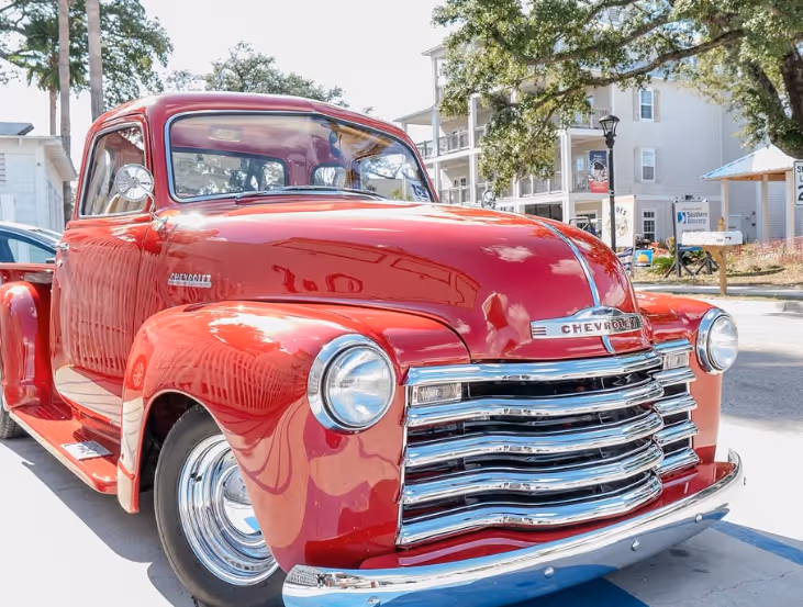 Bright red vintage Chevrolet pickup truck parked on a street during the day.