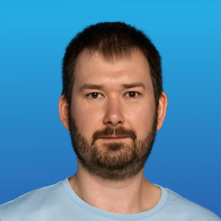 Portrait of a man with short dark hair and beard wearing a light blue shirt against a blue gradient background.