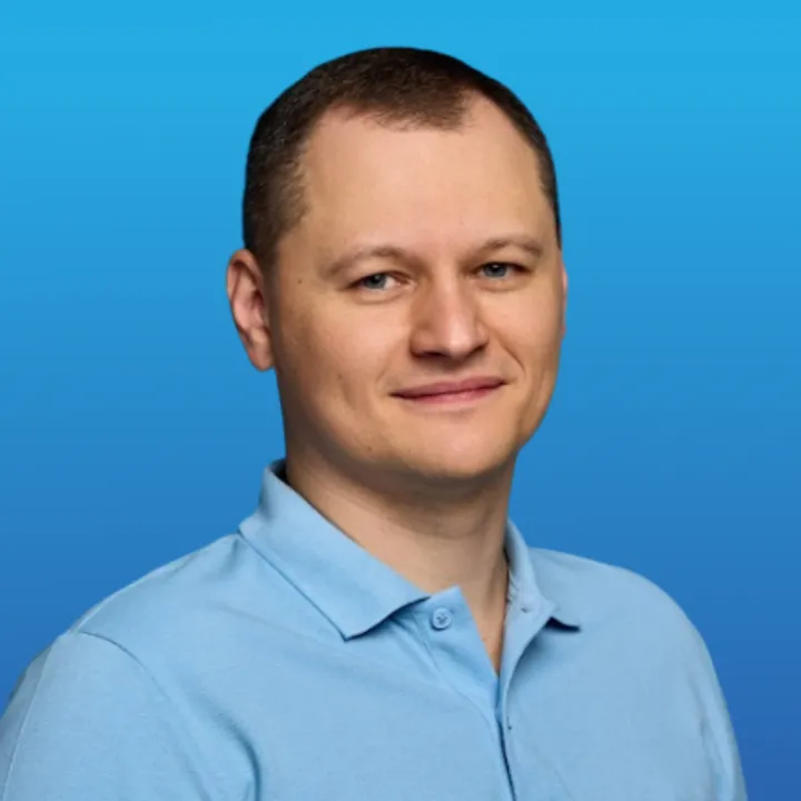 Man with short brown hair wearing a light blue polo shirt against a blue gradient background.