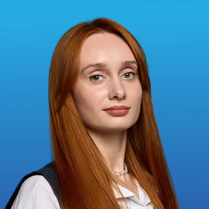 Portrait of a woman with long red hair and light green eyes against a blue gradient background.