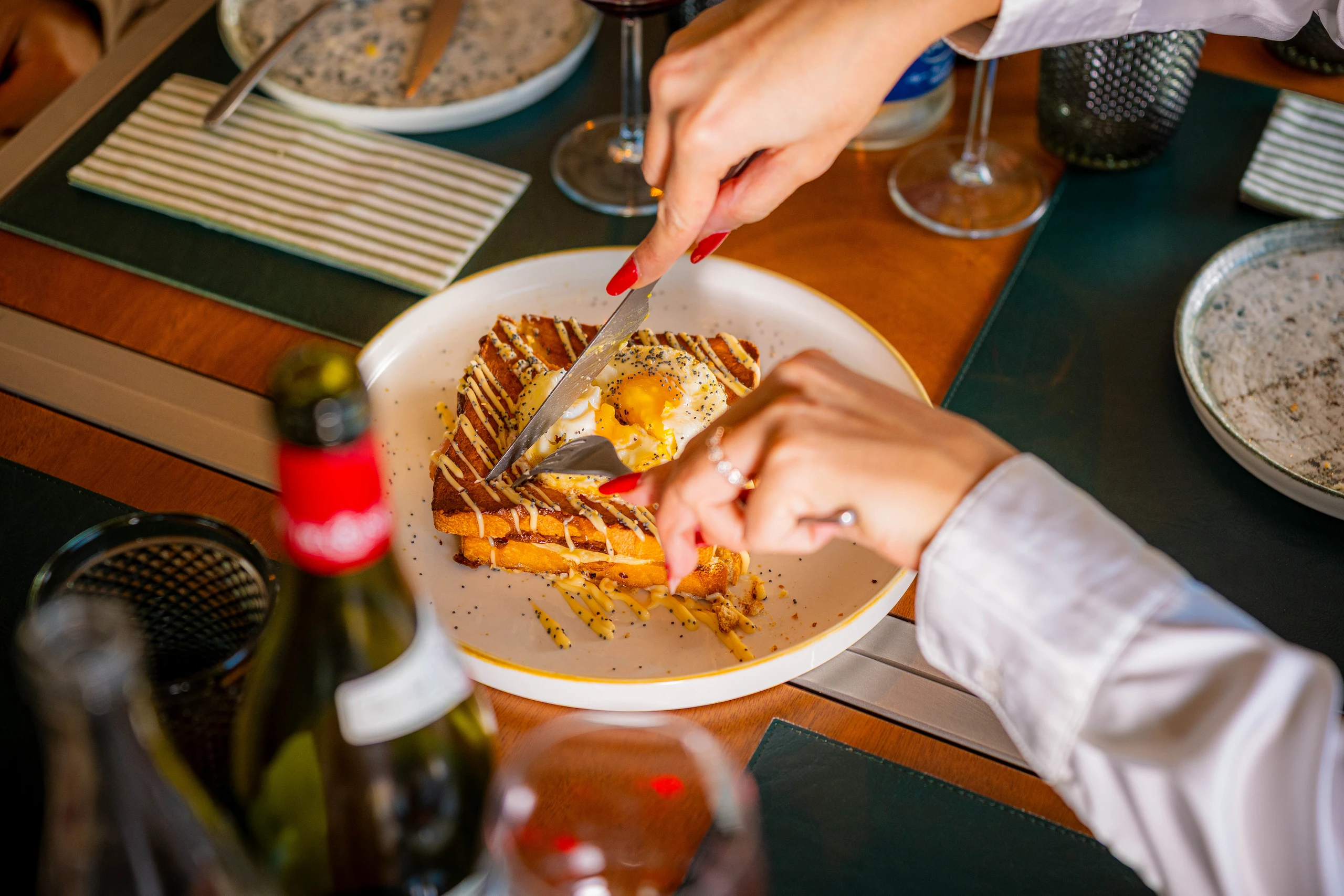 Le Bande Ristorante Cavriana, Shooting Studio Looma. Mani con unghie rosse tagliano una fetta di pane tostato con uovo al tegamino sopra, servito su un piatto bianco in un ristorante.