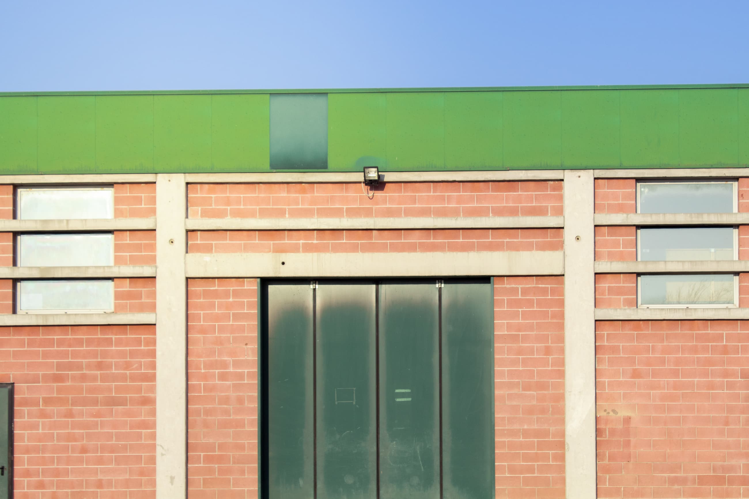 Un paese nuovo, Ceresara, Libro. Facciata di edificio industriale con parete in mattoni rossi, porta verde scuro chiusa e due finestre rettangolari.