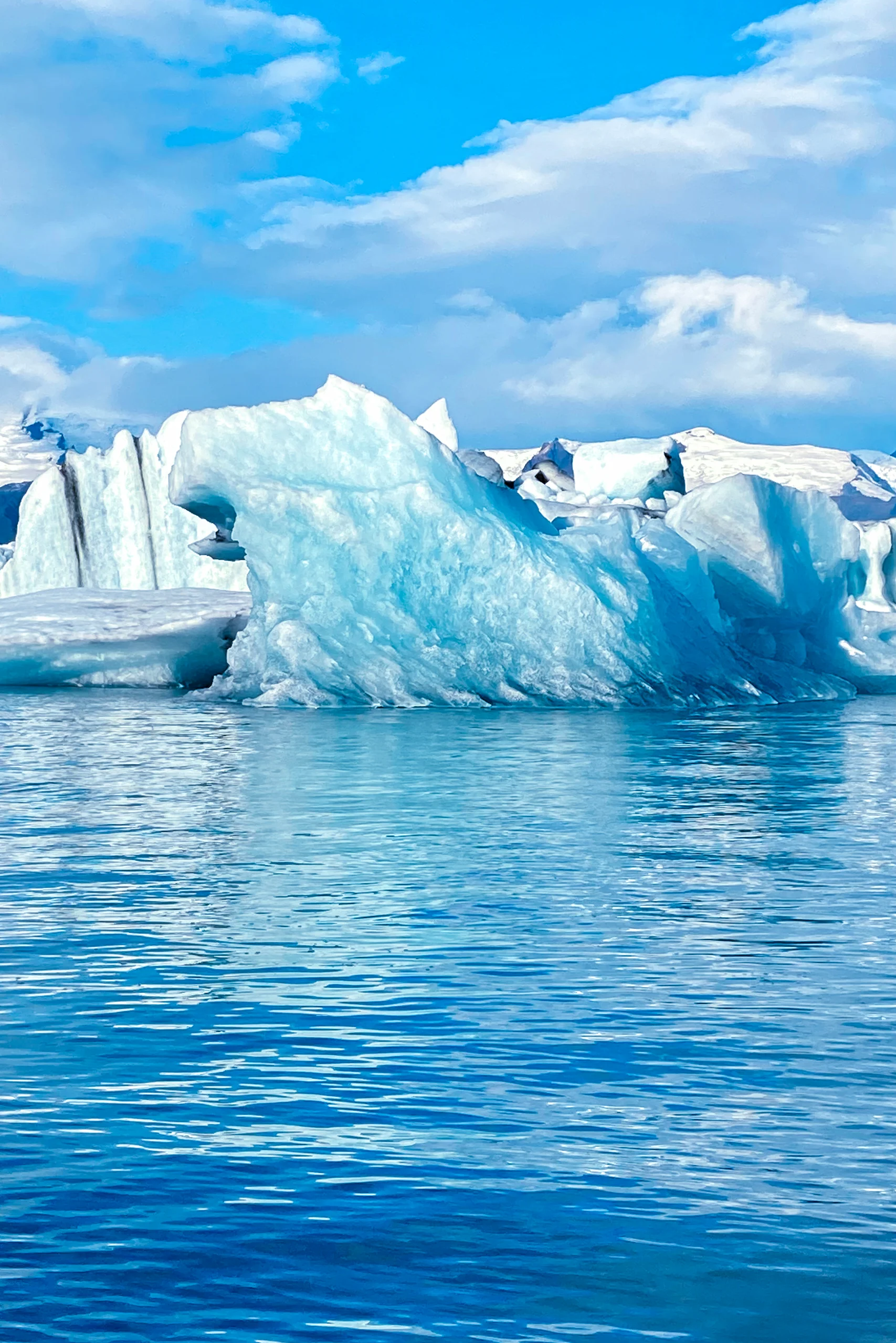 Islanda in auto, libro, Daniel Cortese. Grande iceberg blu galleggiante su acqua calma con cielo parzialmente nuvoloso.