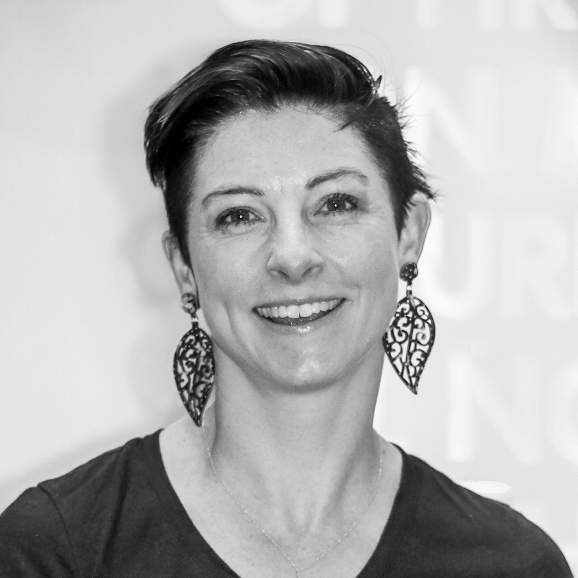 Woman with short dark hair and large intricate leaf-shaped earrings smiling at the camera.
