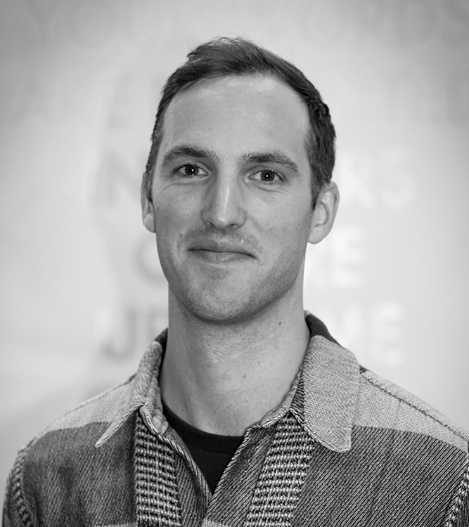 a man wearing a patterned jacket and smiling slightly.