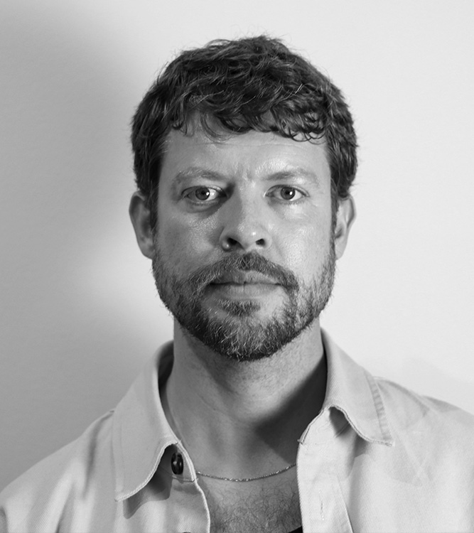 a man with short curly hair, beard, and a buttoned shirt.