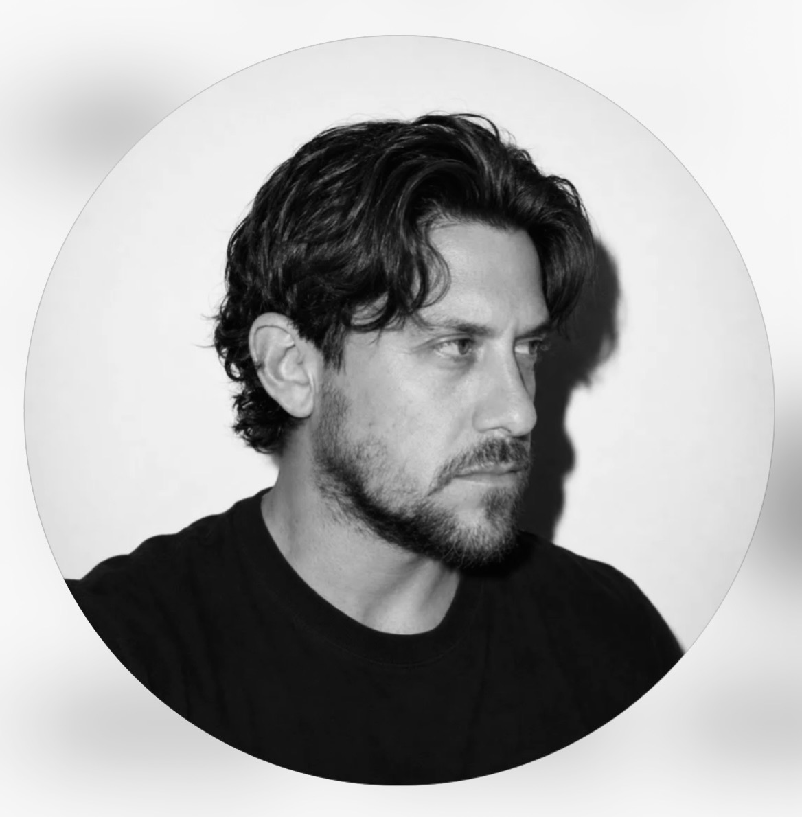 a man with dark hair and beard wearing a black shirt looking to the right.