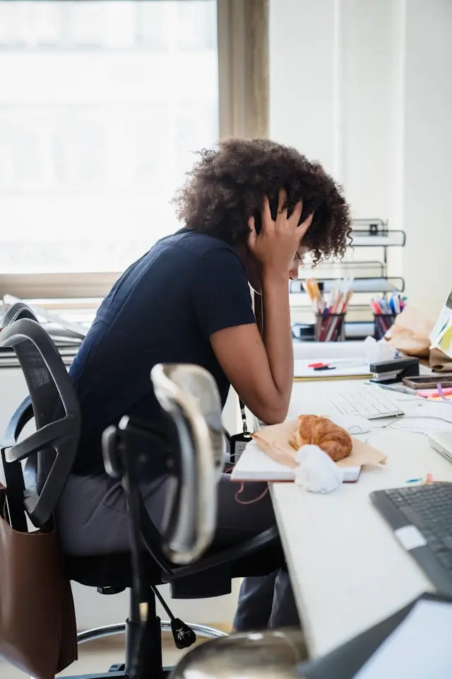 Personne assise à un bureau, tenant sa tête entre ses mains, semblant stressée ou fatiguée