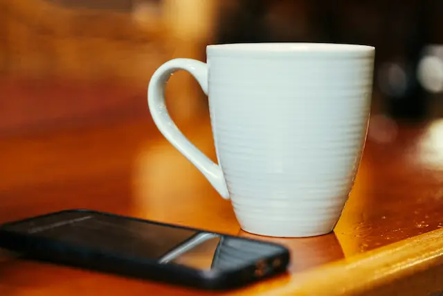 Une tasse blanche et un smartphone posé sur une table en bois.
