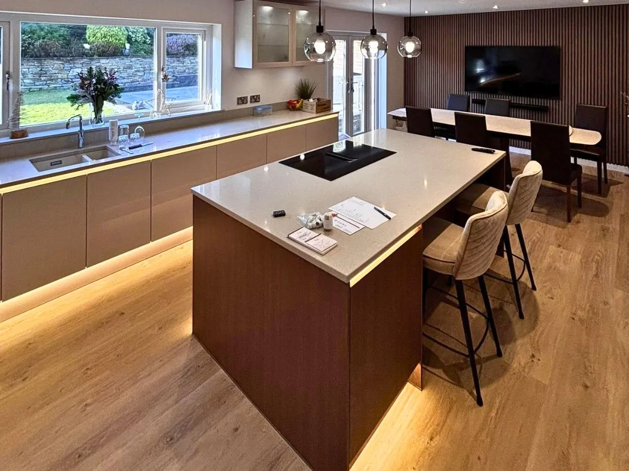 Modern kitchen with large island, bar stools, dining table, and under-cabinet lighting.