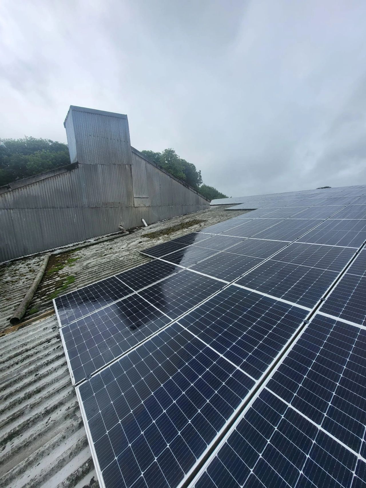Solar panels installed on an old corrugated metal roof of a rustic building under a cloudy sky.