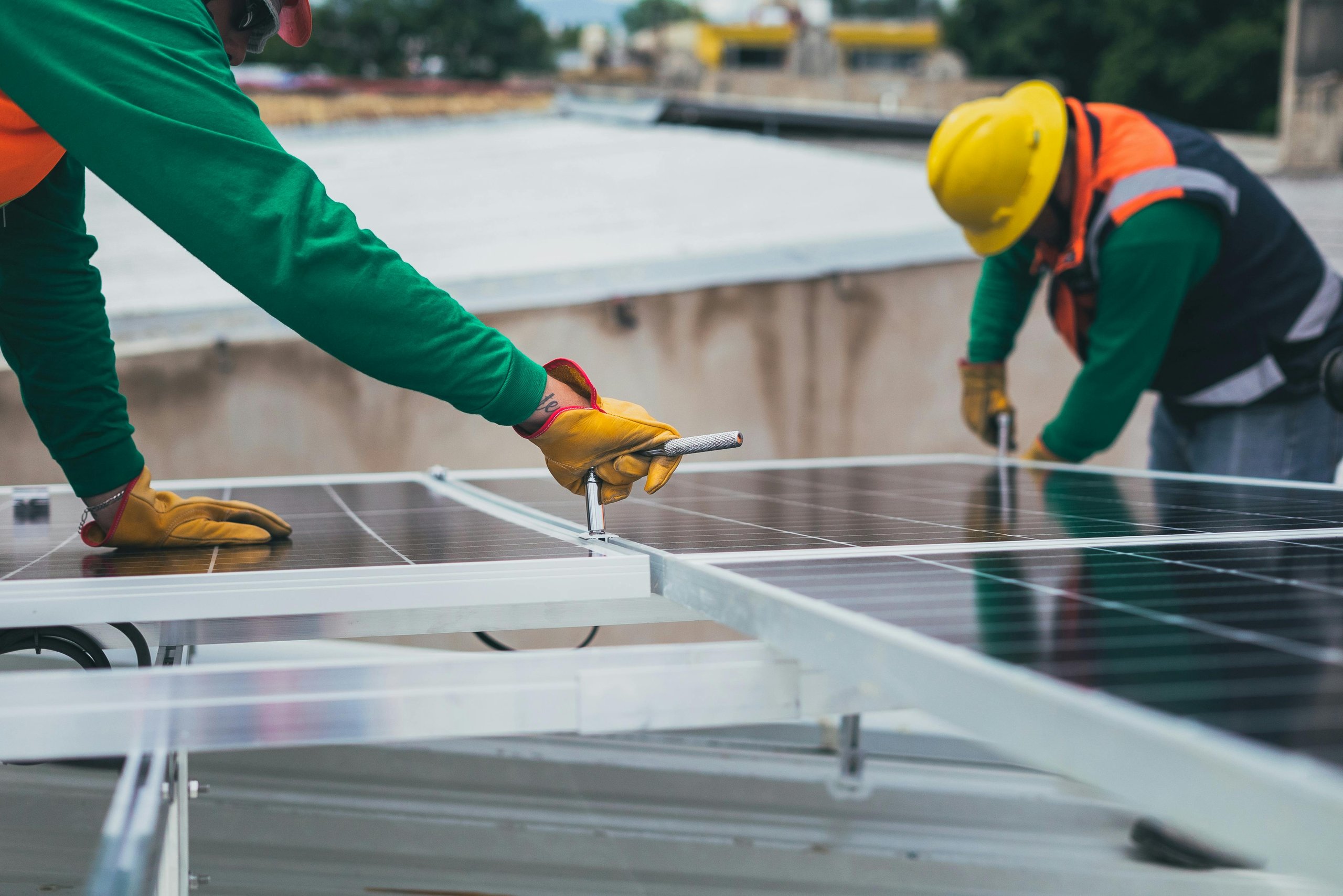 Two workers wearing gloves and safety gear installing solar panels on a rooftop.