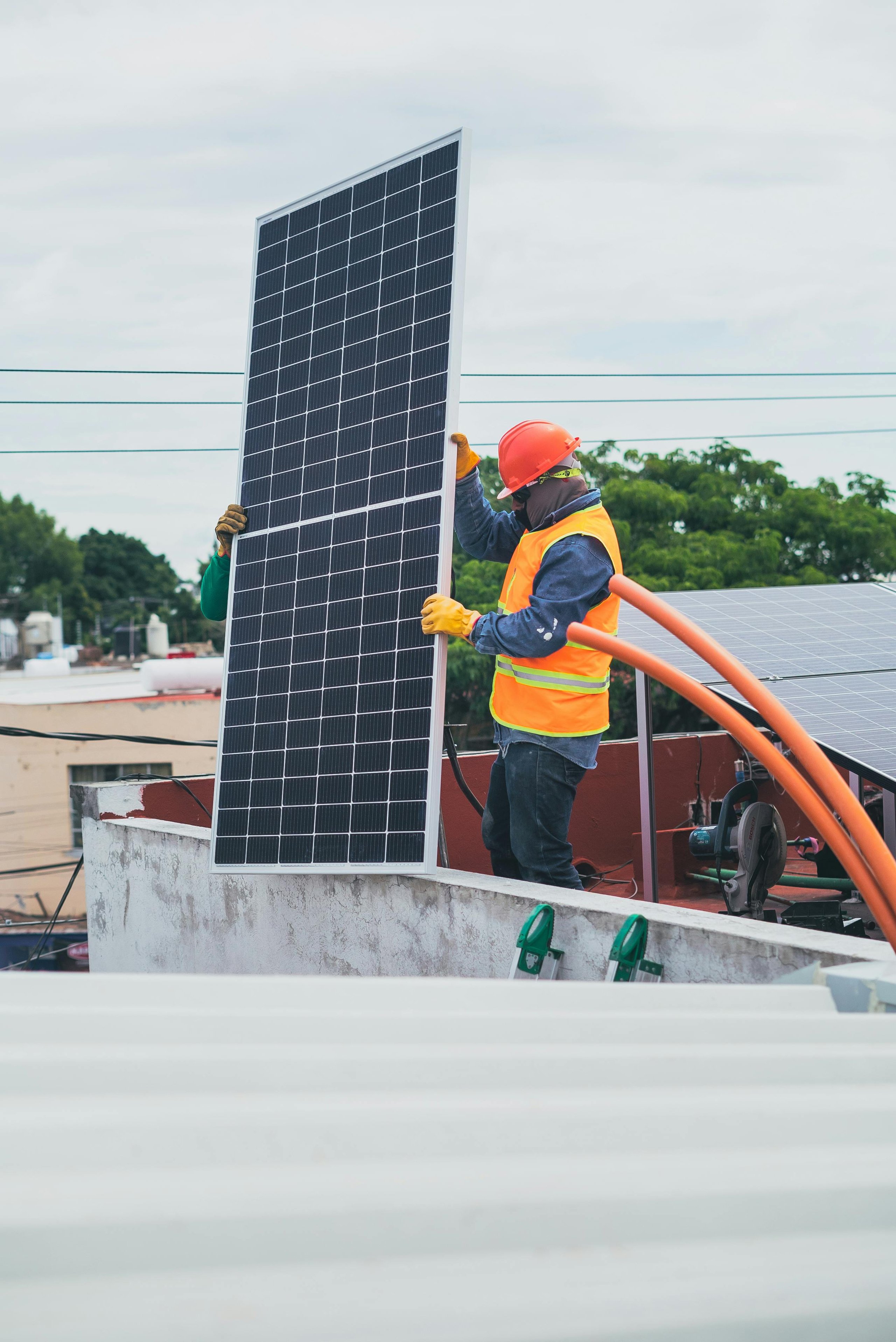 Two workers wearing safety gear installing a solar panel on a rooftop.