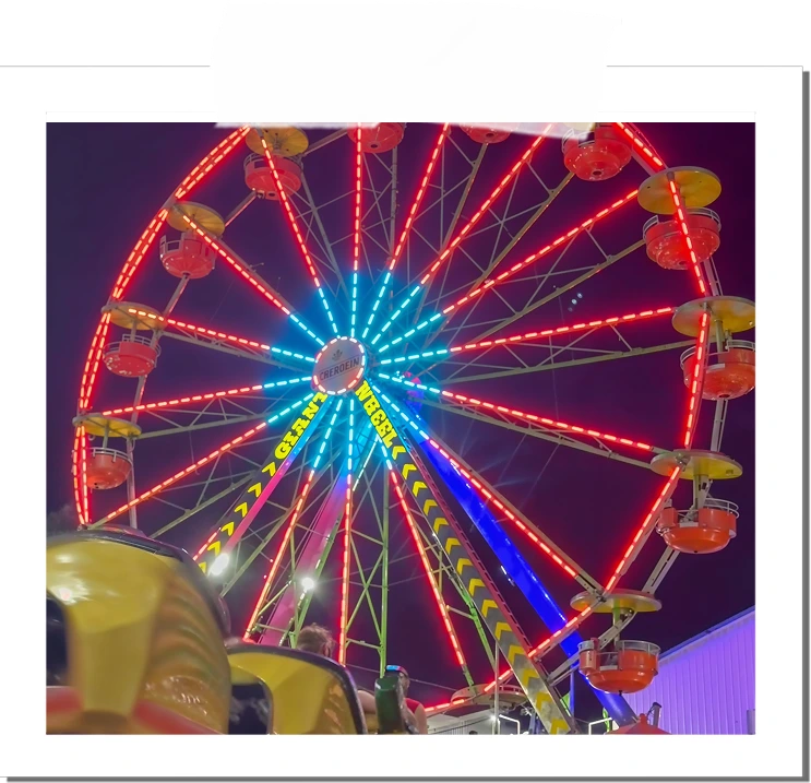 Ferris wheel lit with red, blue, and yellow lights at night with people seated nearby.